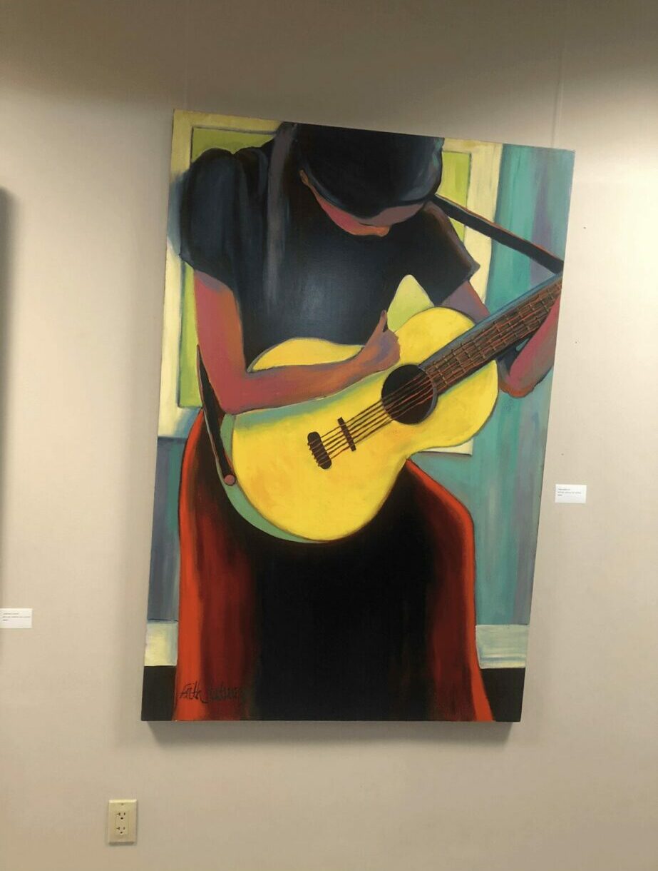 Painting of a person playing a yellow guitar, wearing a dark shirt and red pants, with a dark background.