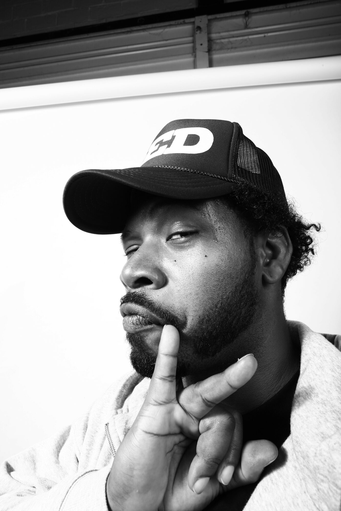 Young man wearing a cap, resting his head on a surface, with a hand touching his face, in black and white.
