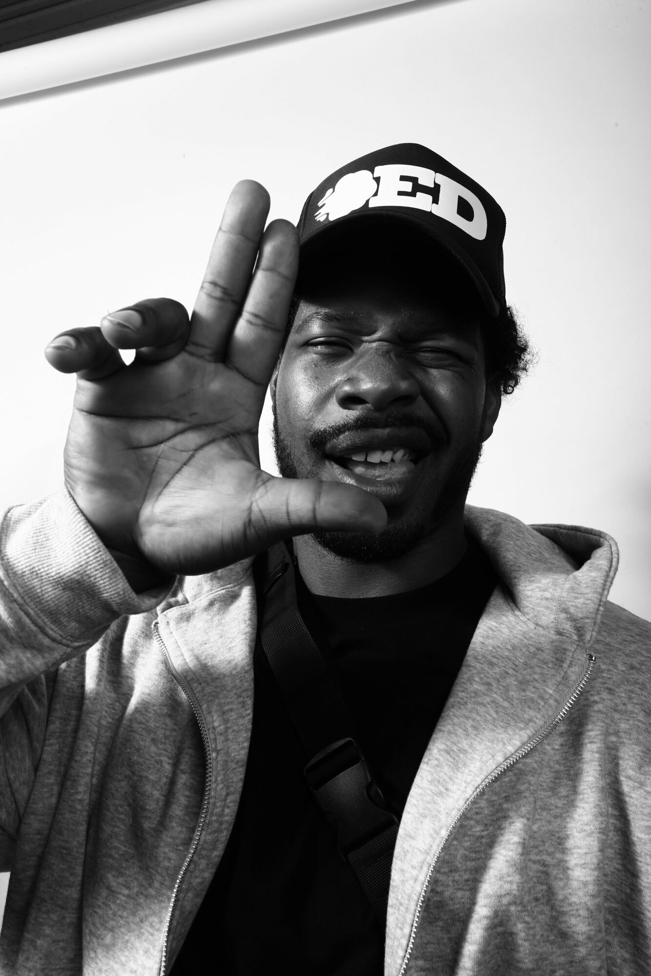 Person making a peace sign with hand near face, smiling, wearing a headband and hoodie, indoors.