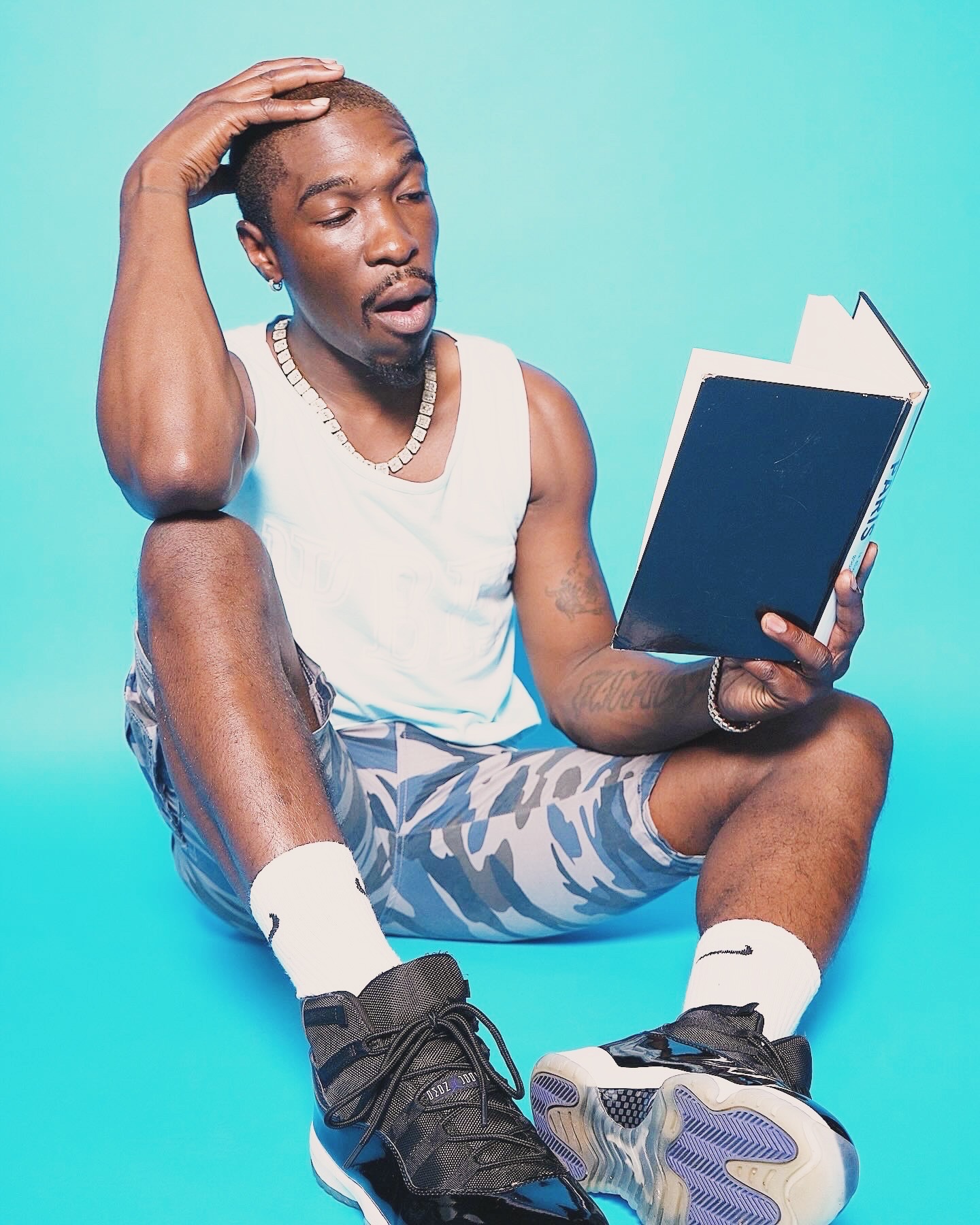 Person sitting with legs crossed, reading a book, against a blue background.