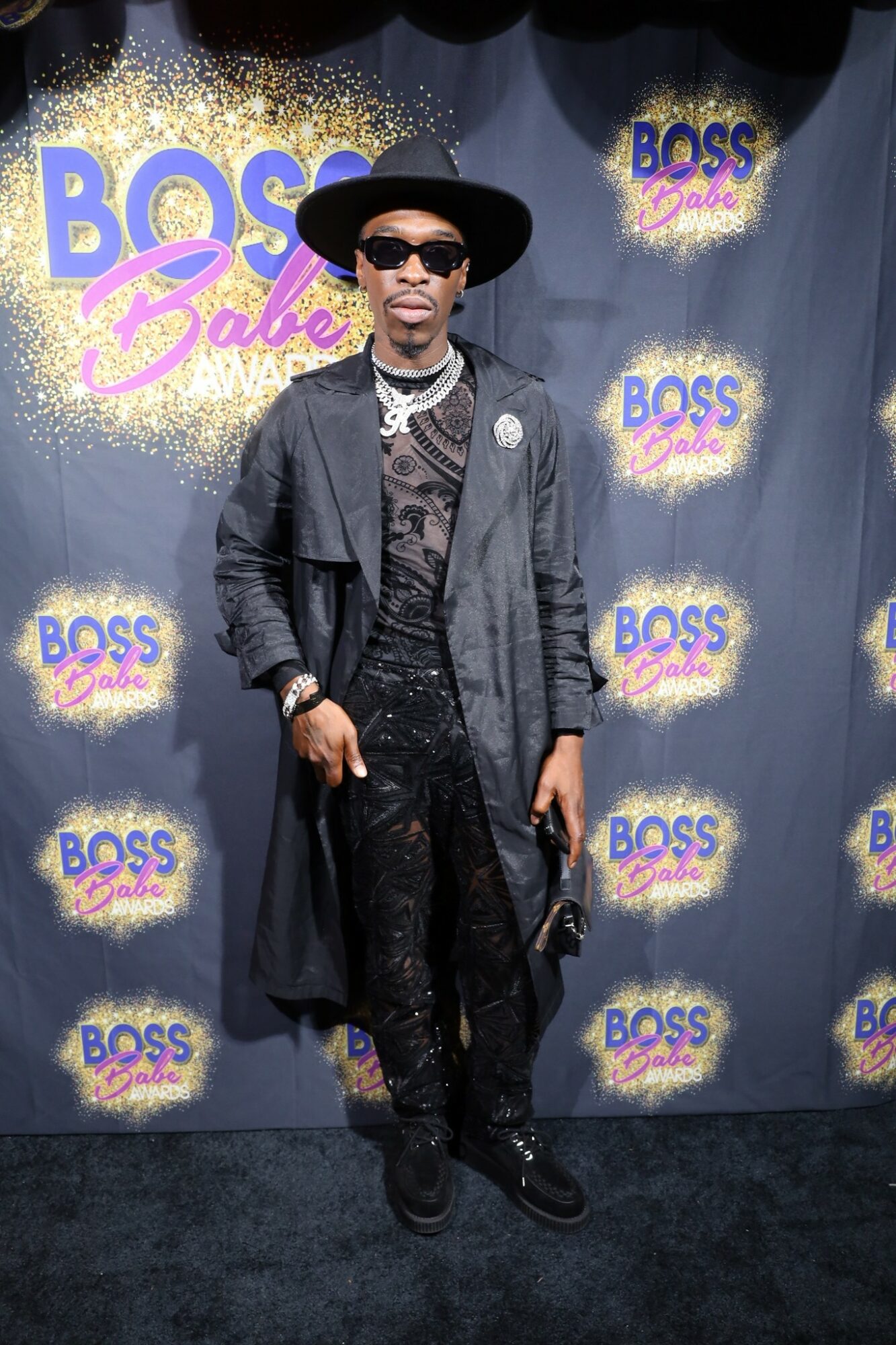 Person wearing sunglasses, hat, and dark clothing standing in front of a BOSS Baby backdrop.