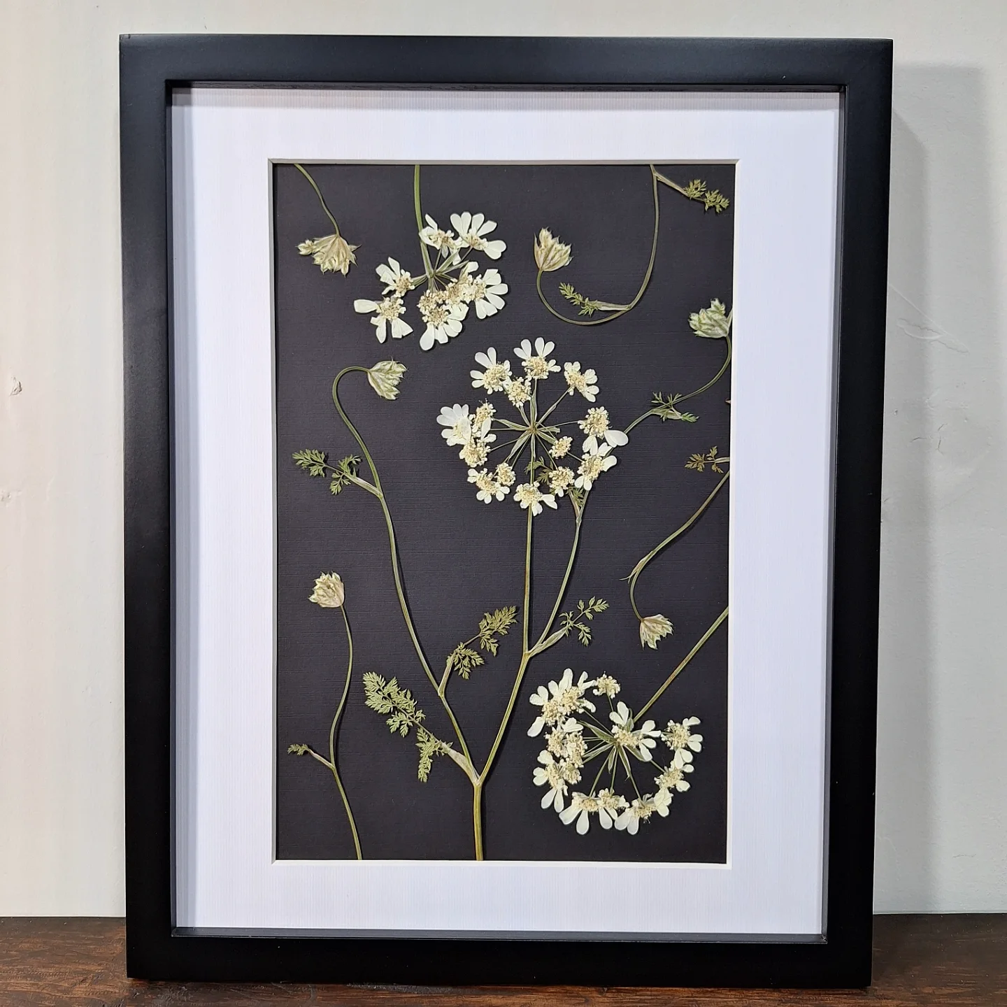 Framed artwork of white flowers with green stems on a dark background, in a black frame with white matting.