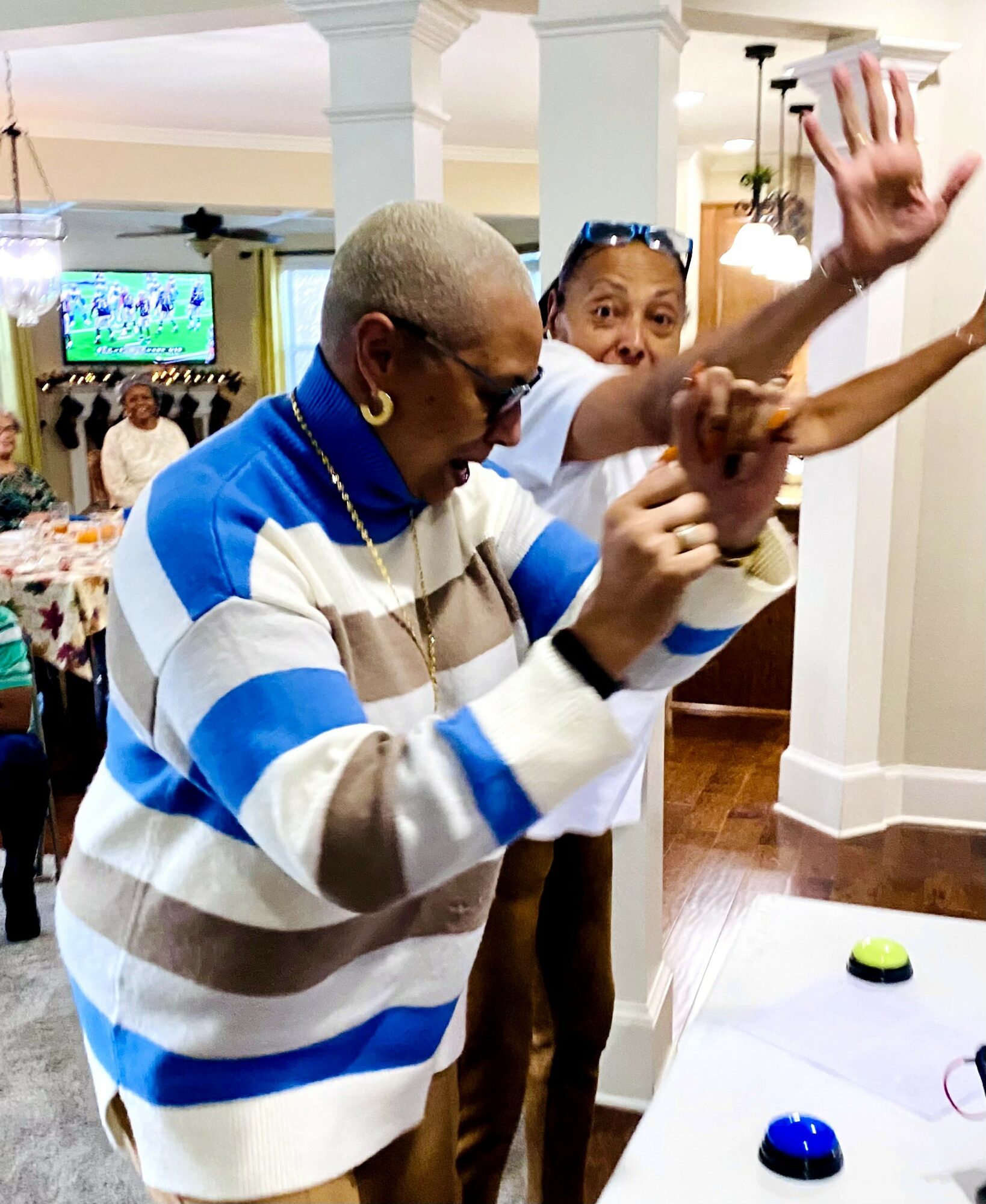 Two people dancing indoors, one with sunglasses and striped sweater, the other with glasses and white shirt, in a lively setting.