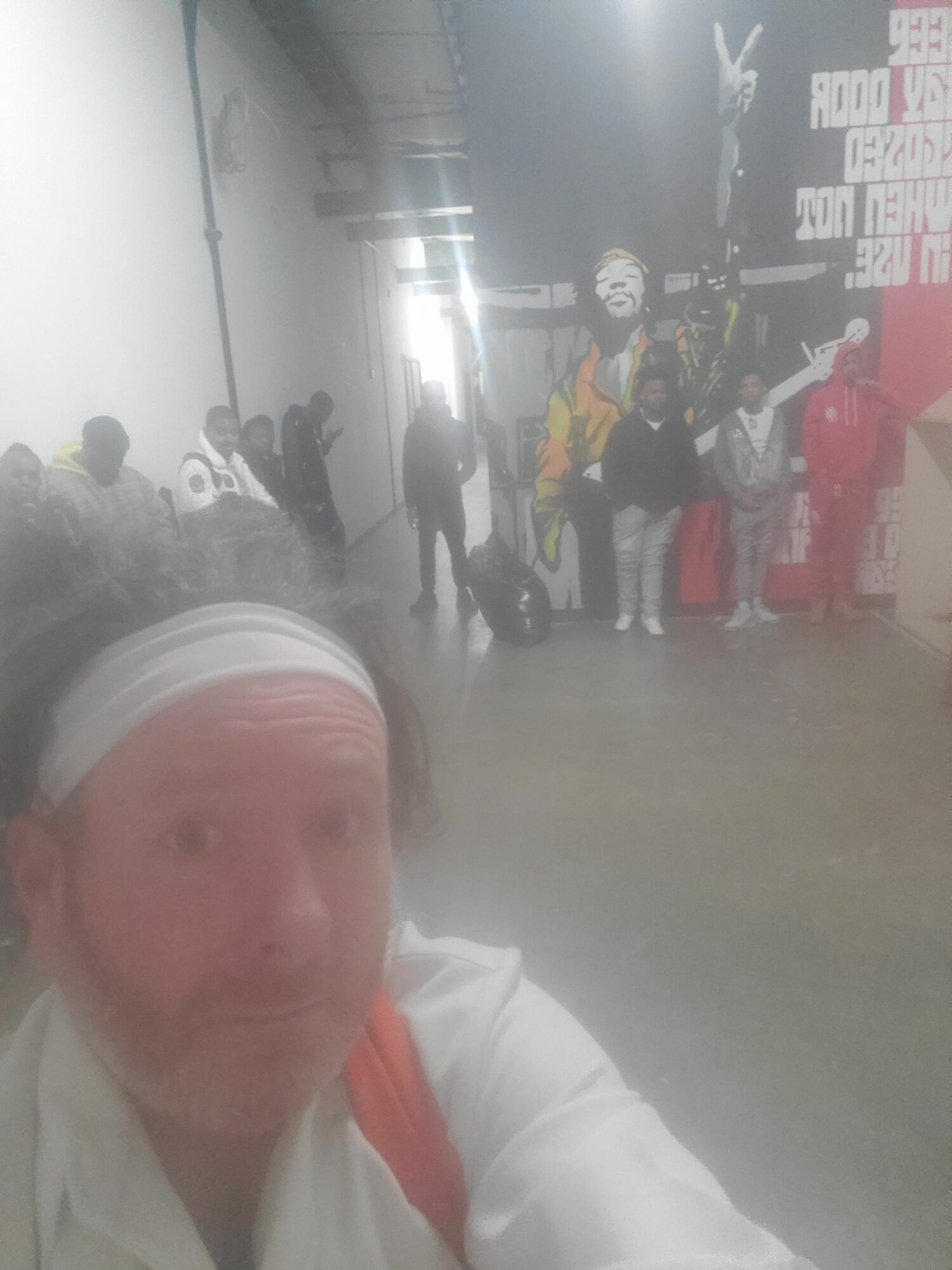 Person wearing a white head covering and white clothing, with a red strap, in a busy indoor setting with people and posters.