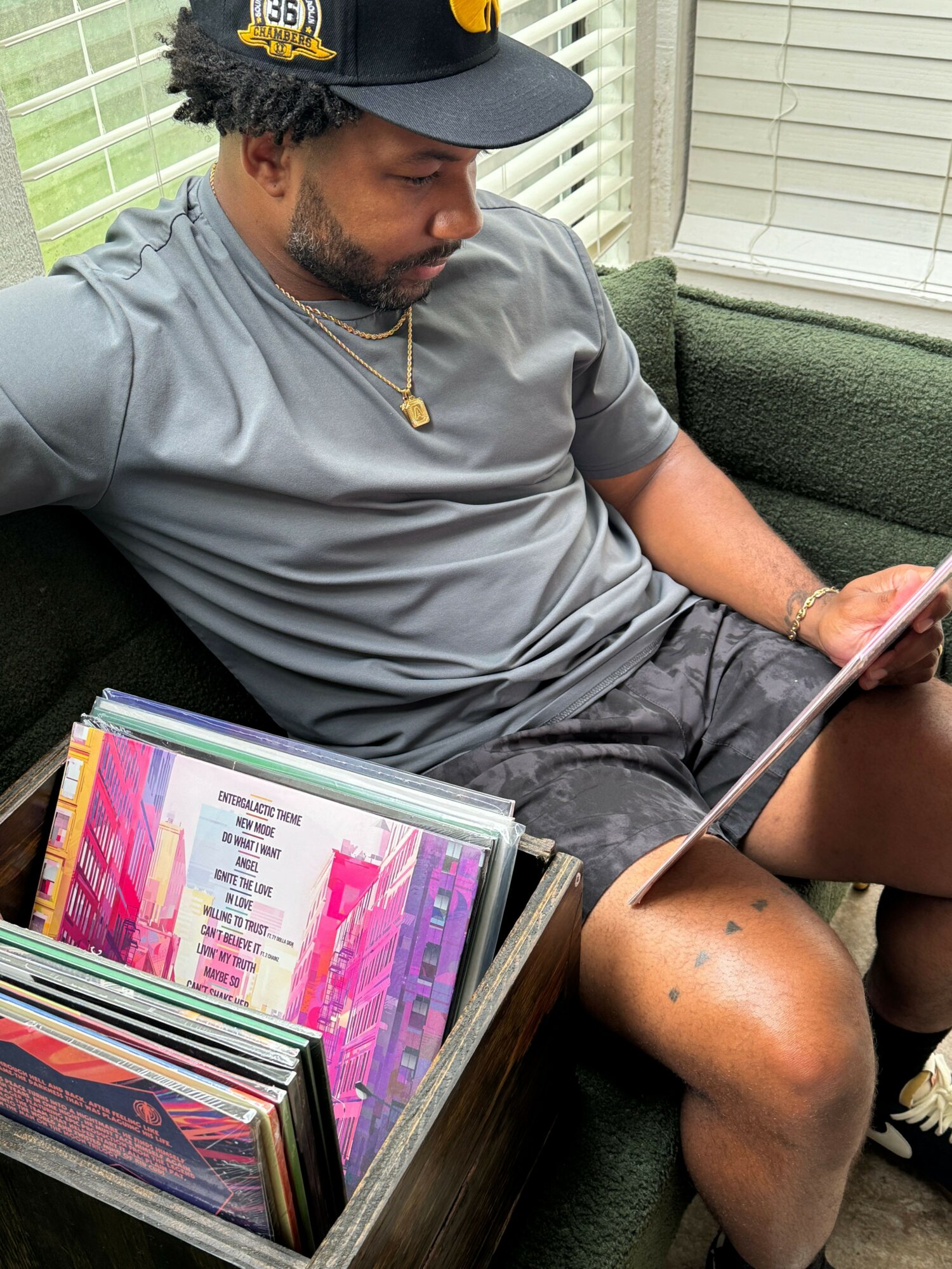 Person lying on a couch reading a book, with a laptop nearby, in a room with a window and blinds.
