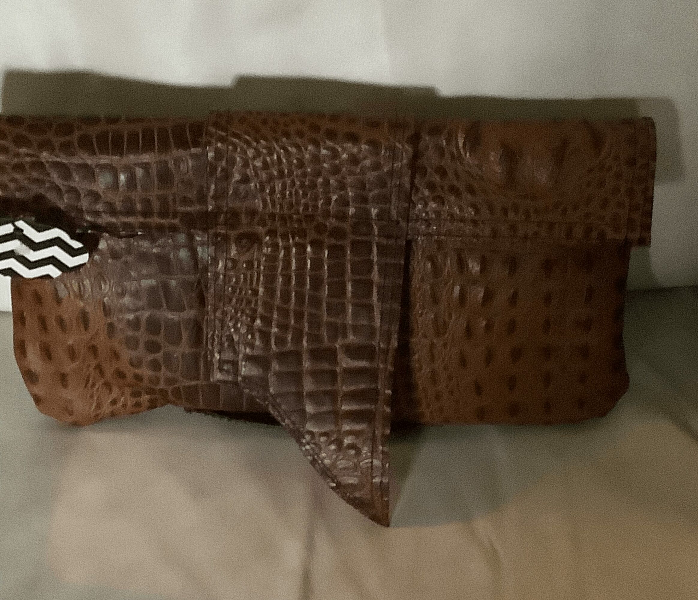 Brown crocodile-patterned leather wallet with a flap, placed on a light surface.
