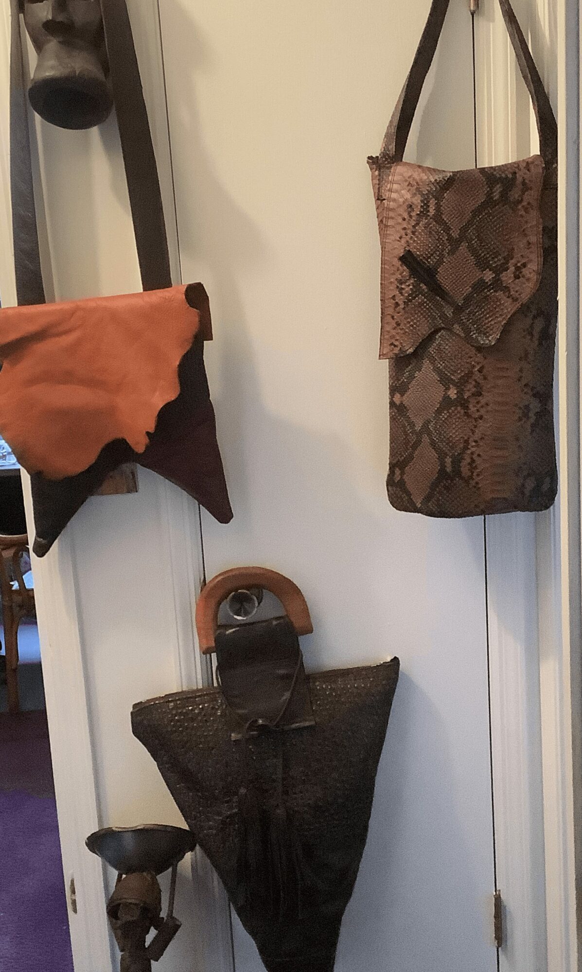 Two bags hanging on a wall, one with a snake skin pattern and the other with a dark textured surface.