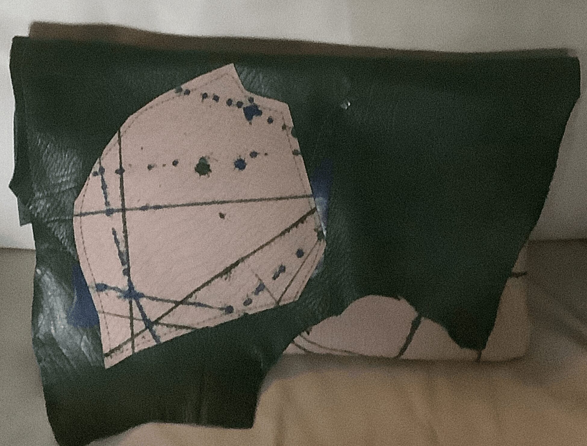 Fragment of dark green material with a circular cutout and blue ink splatters, placed on a light surface.