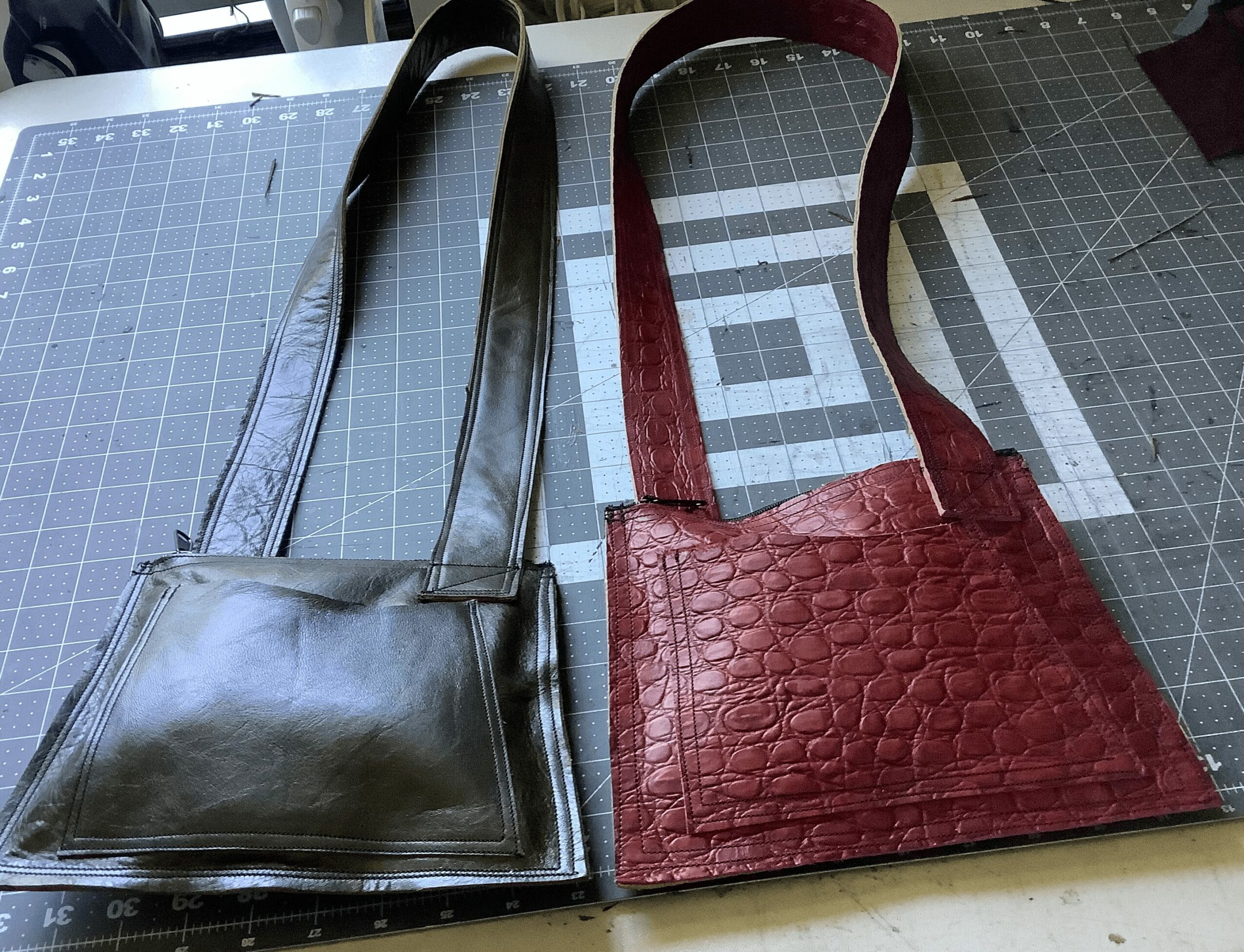 Two handbags, one black and one red, placed on a cutting mat with grid lines and measurement markings.