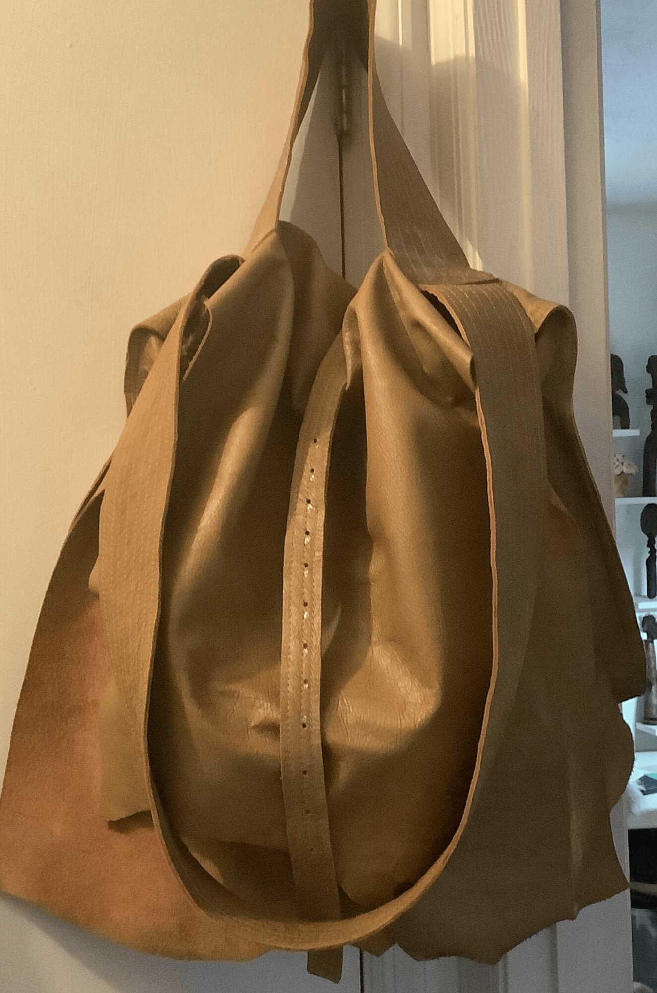 Two beige and brown bags hanging on a hook near a window, with a cityscape visible outside.