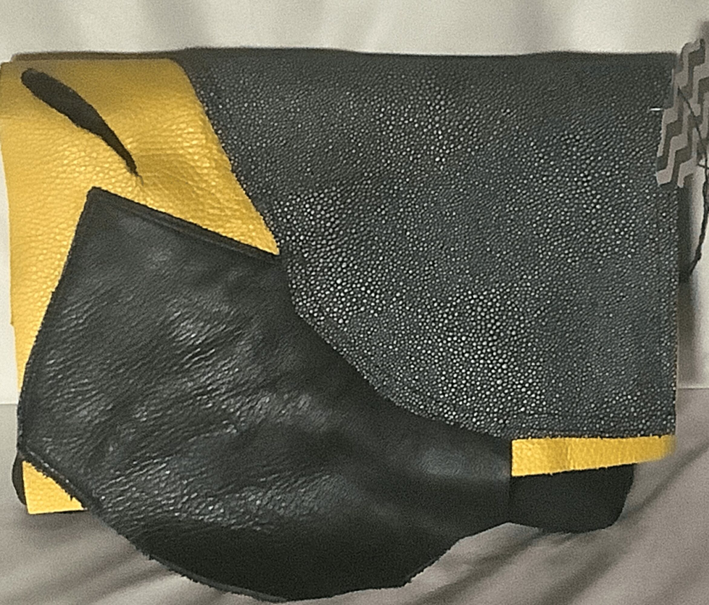 Black leather bag with a yellow and black textured flap, resting on a surface. The bag is partially open, showing its interior.