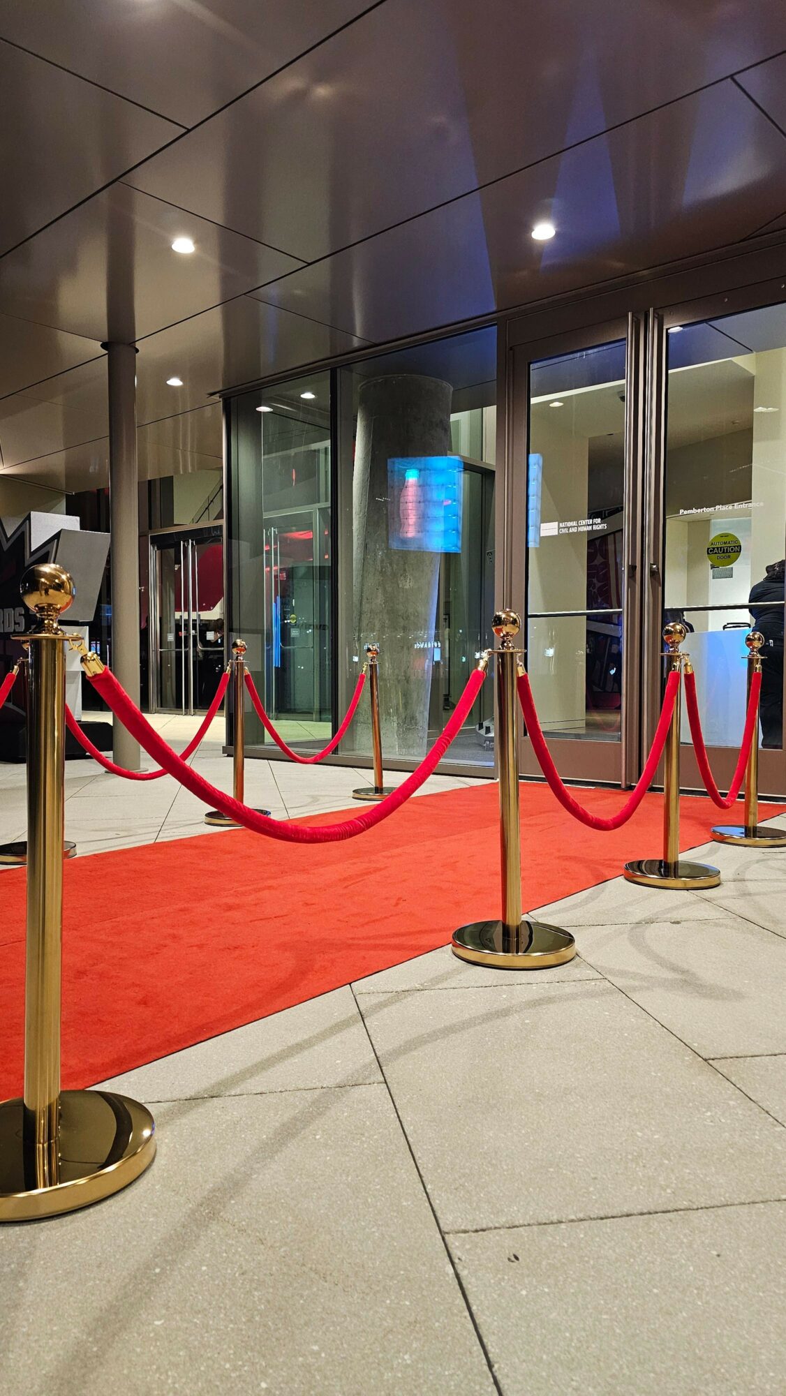 Red velvet rope barriers with gold stanchions create a pathway outside a building entrance.