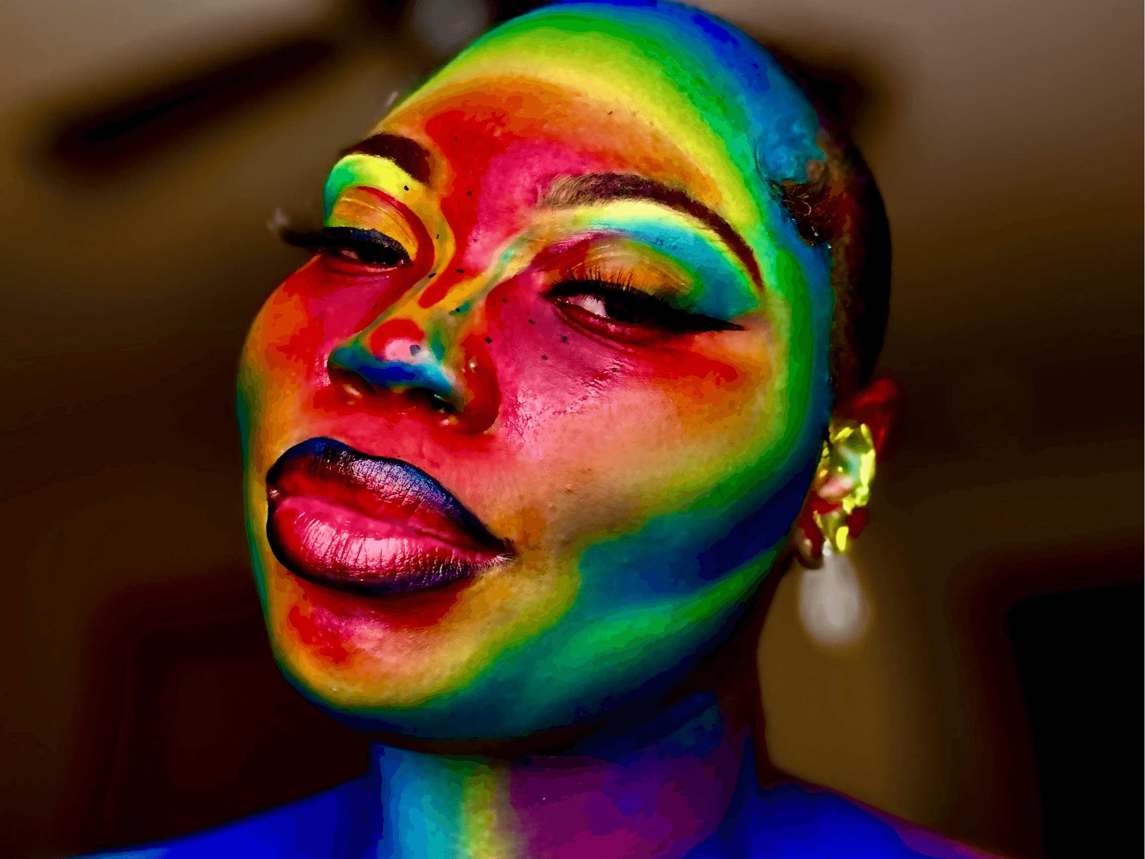 Close-up of a person with rainbow-colored face paint, eyes partially closed, lips slightly parted, and a earring visible.