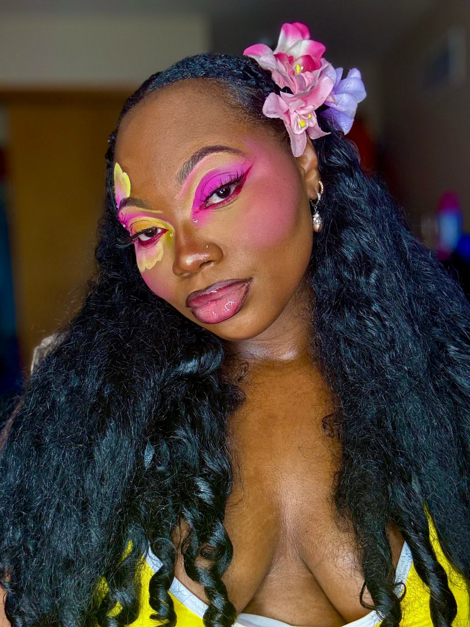 Woman with vibrant pink, yellow, and purple eye makeup, floral hair accessories, and long black curly hair.