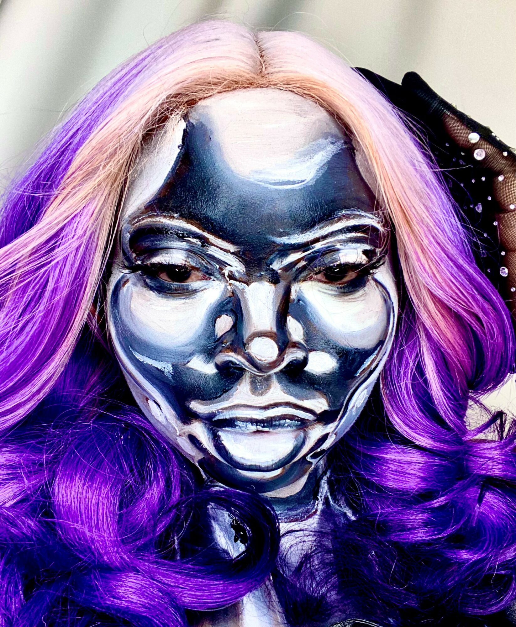 Person with metallic face paint and long, wavy hair dyed purple and pink, looking directly at the camera.
