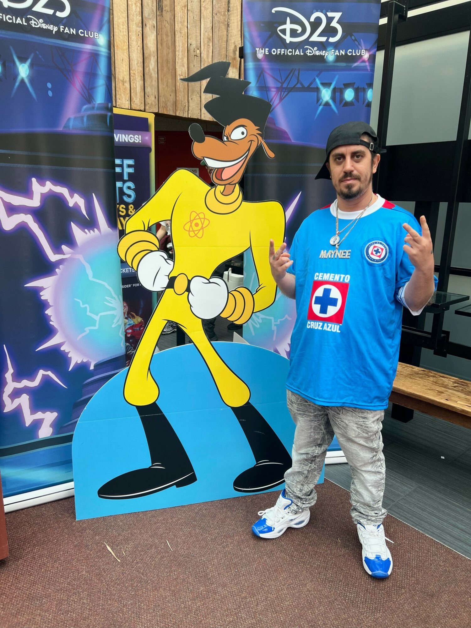Young boy in a blue medical-themed costume standing next to a cartoon character cutout, with a backdrop of a science exhibit.