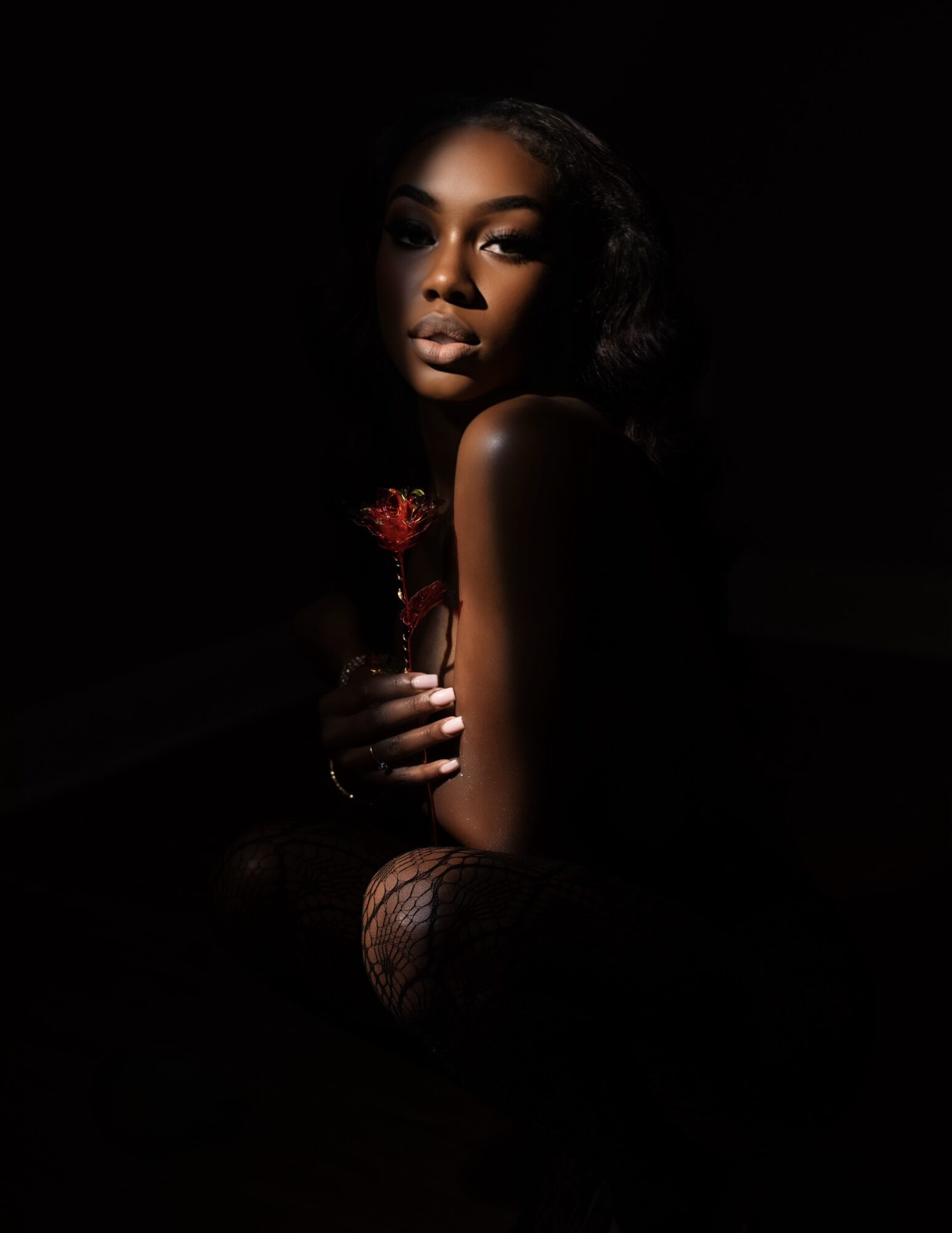 Woman with dark hair holding a red flower, illuminated face, dark background, contemplative expression.