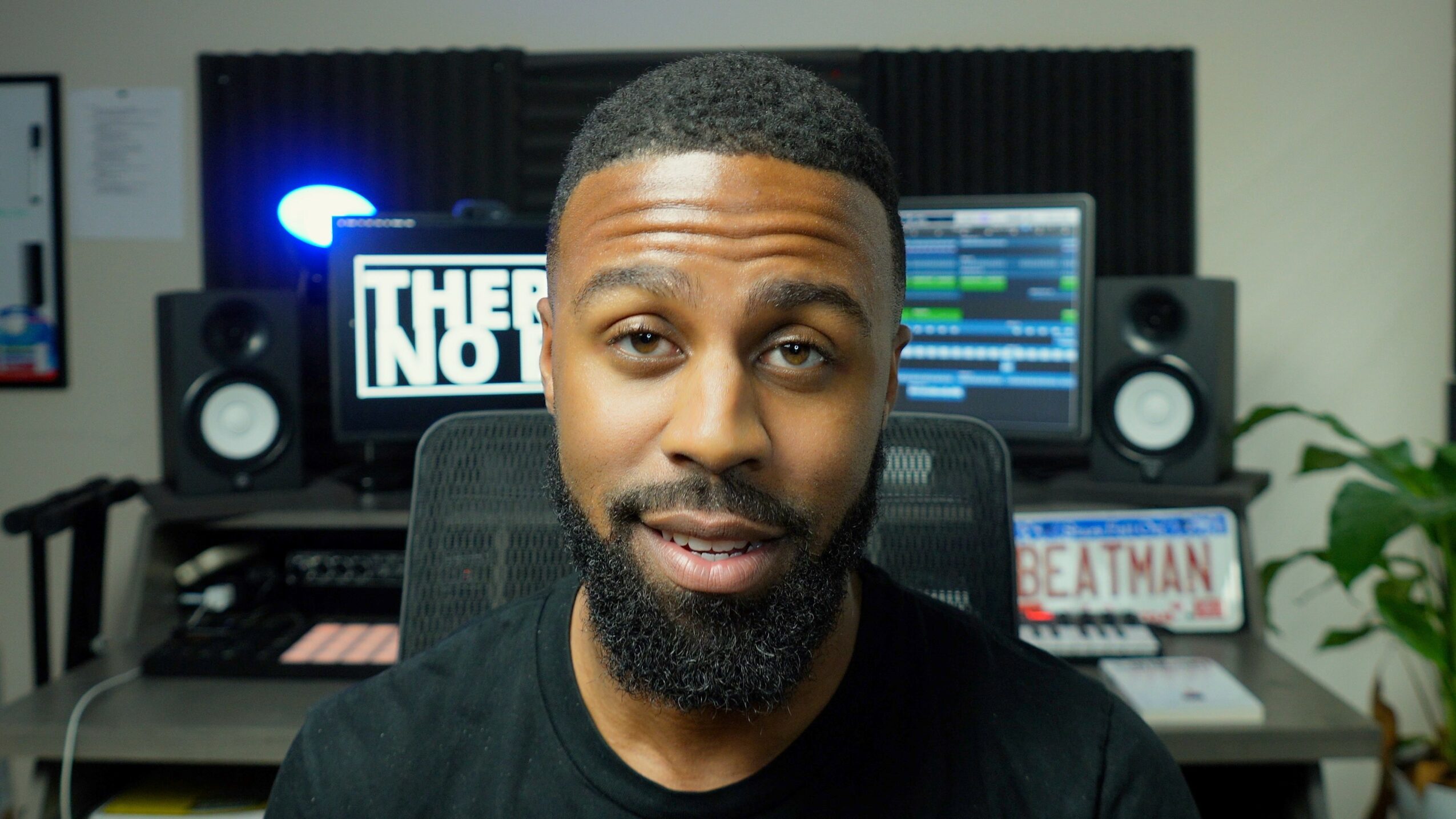 Man with short hair and beard in a recording studio with monitors and equipment behind him.