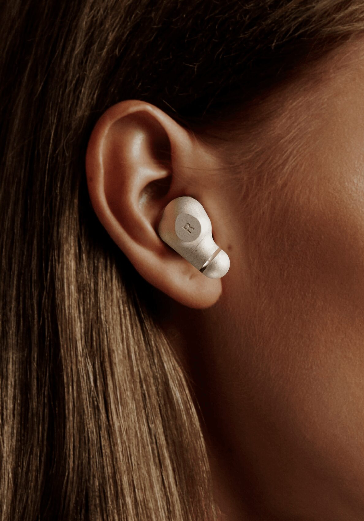 Close-up of a person's ear with a white wireless earbud inserted, showing hair and skin details.