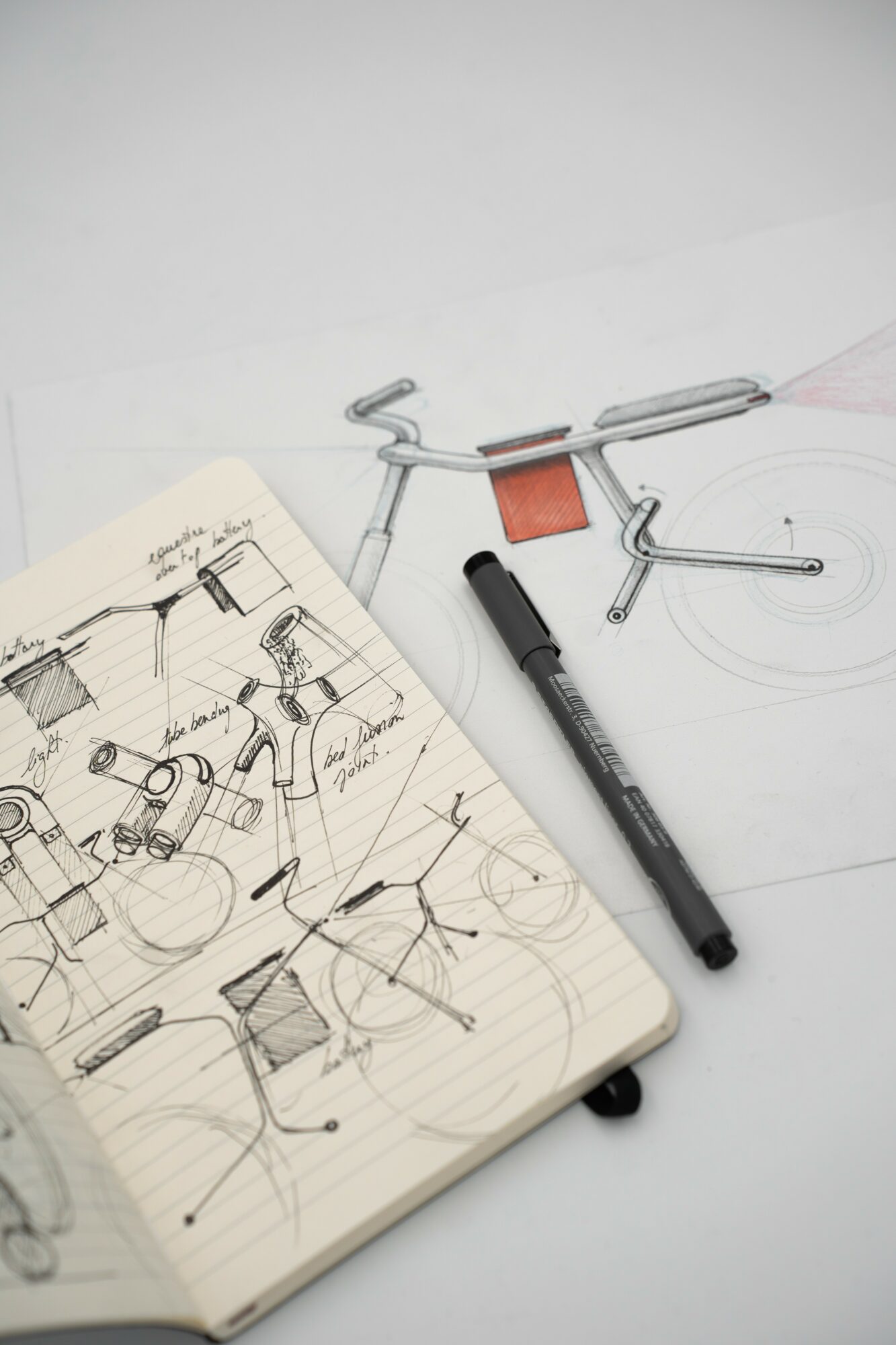 Open sketchbook with technical drawings, a black marker, and metal tools on a white surface.