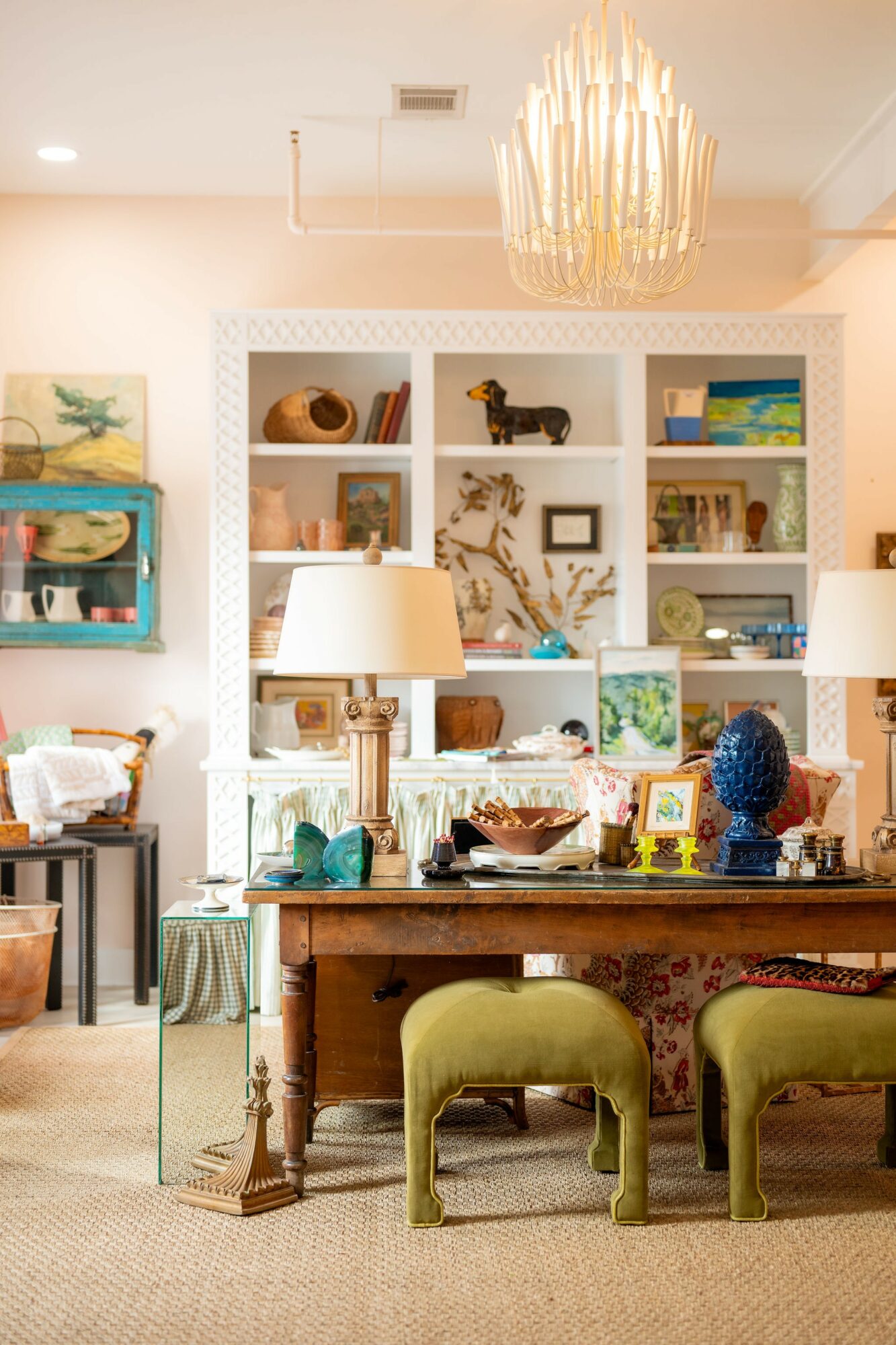 Living room with shelves, lamps, and decorative items, including a chandelier and a table with green chairs.