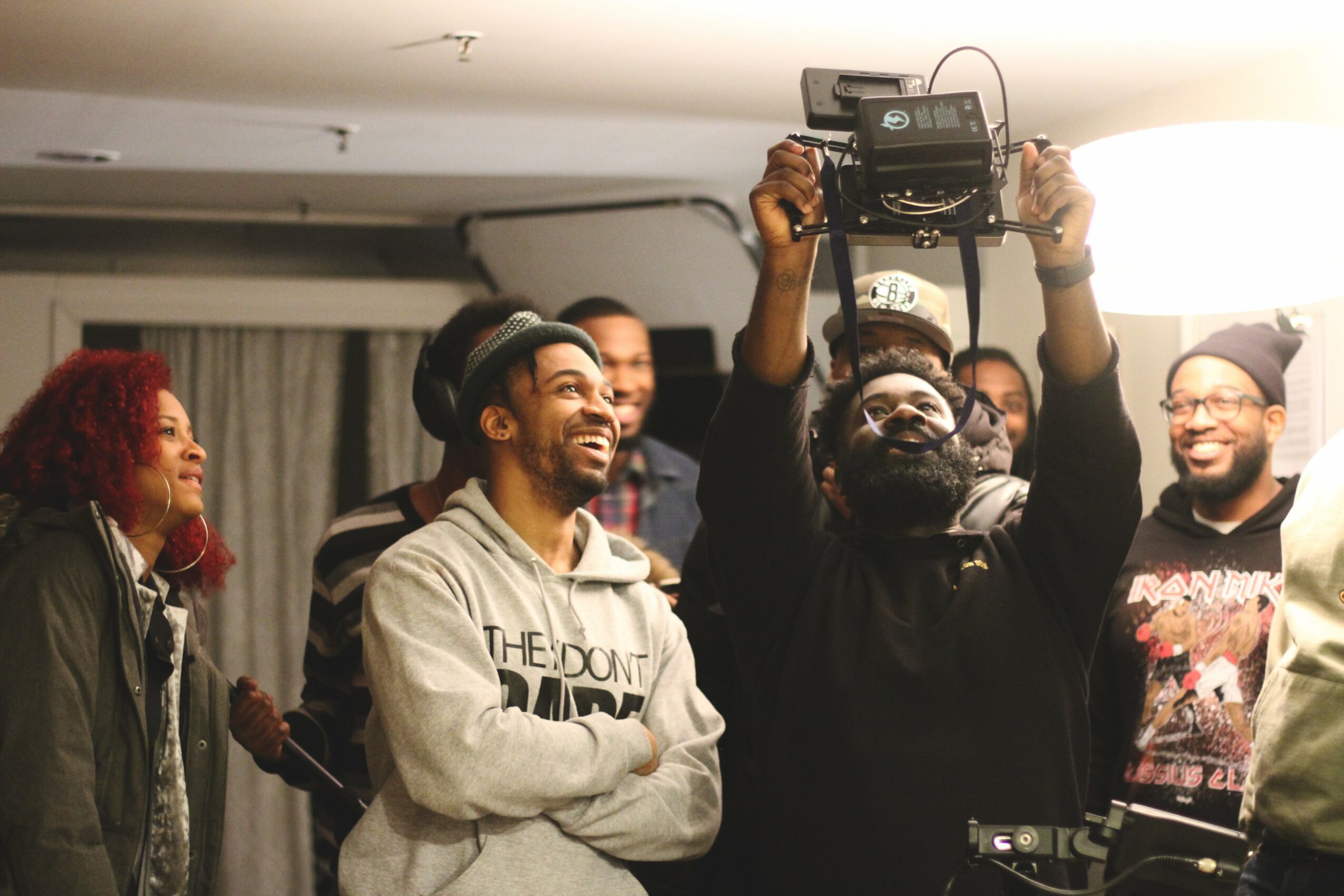 Group of people smiling and laughing indoors, one person holding a radio above their head, others watching and smiling.