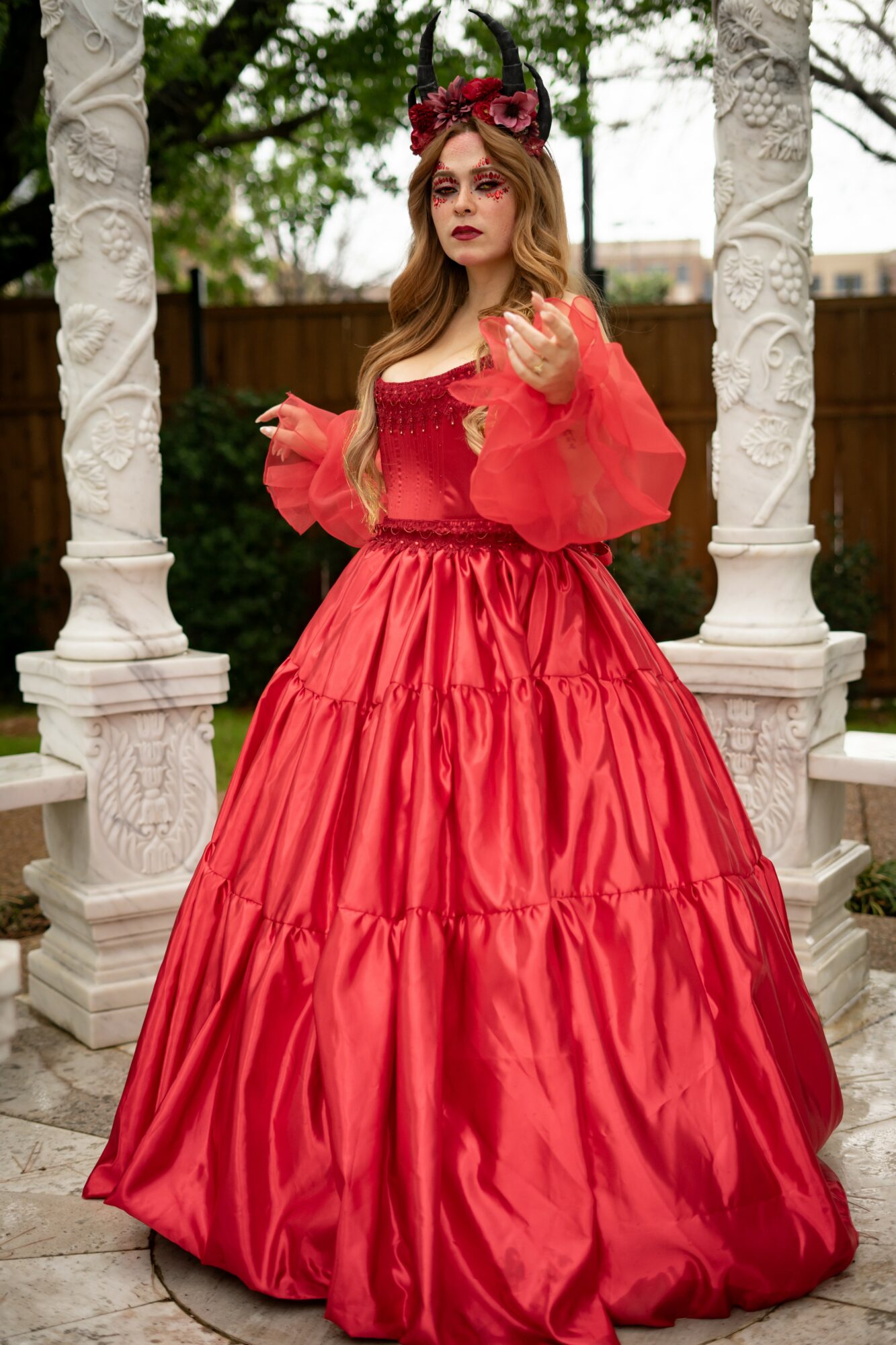 Young woman in a red dress with puffy sleeves and a full skirt, standing between white columns outdoors.
