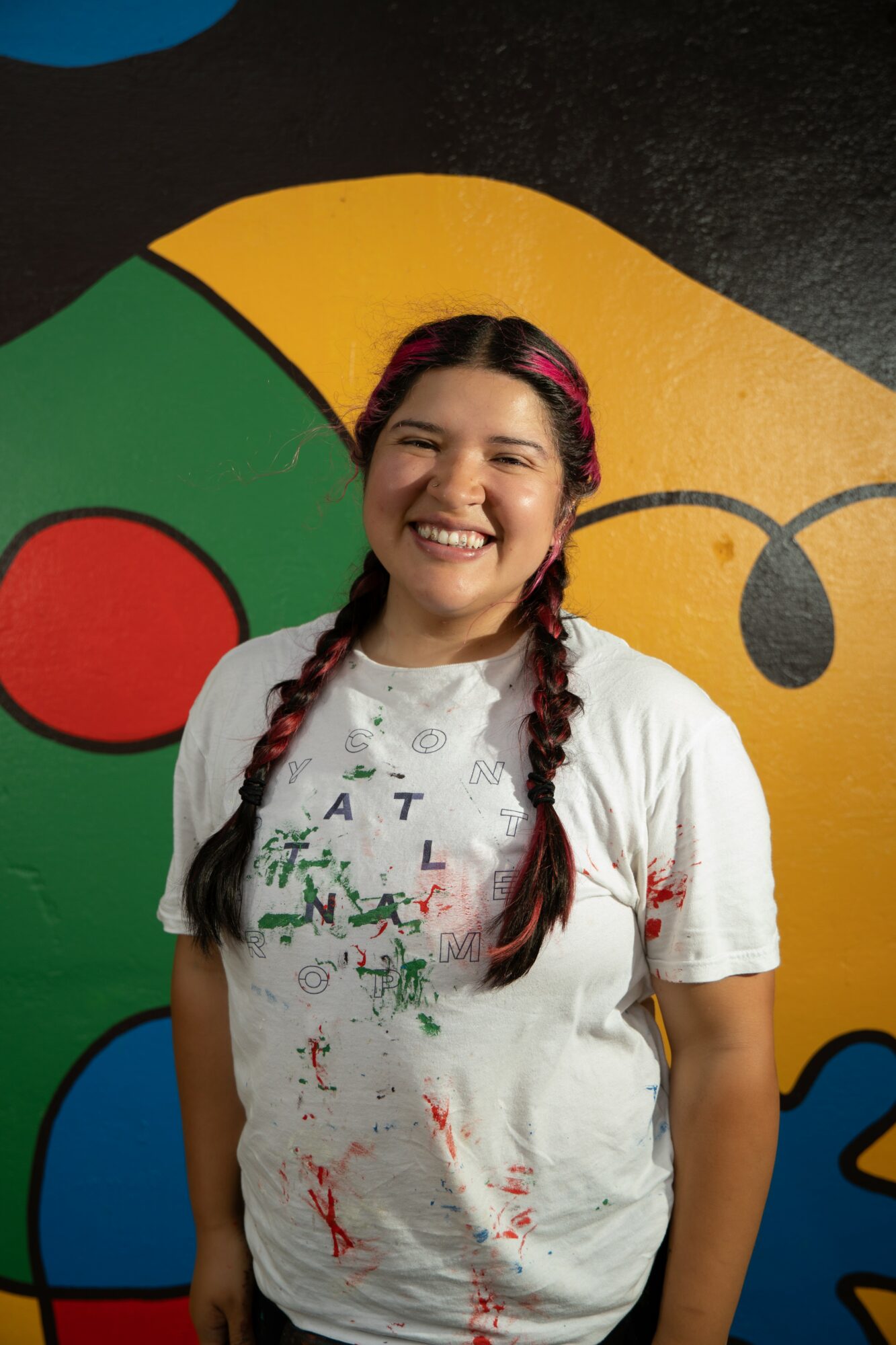 Smiling girl with braided hair and a white shirt stands in front of a colorful background.