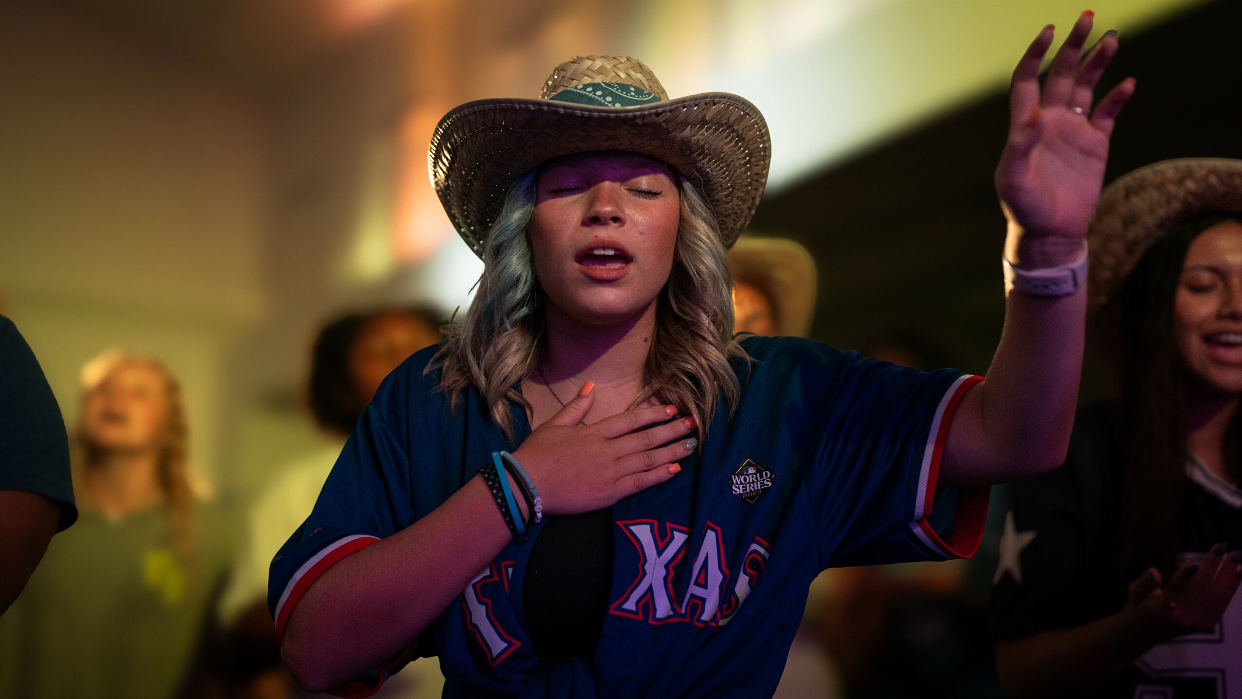 Woman wearing a cowboy hat and Texas jersey with eyes closed, hand on chest, in a group setting.