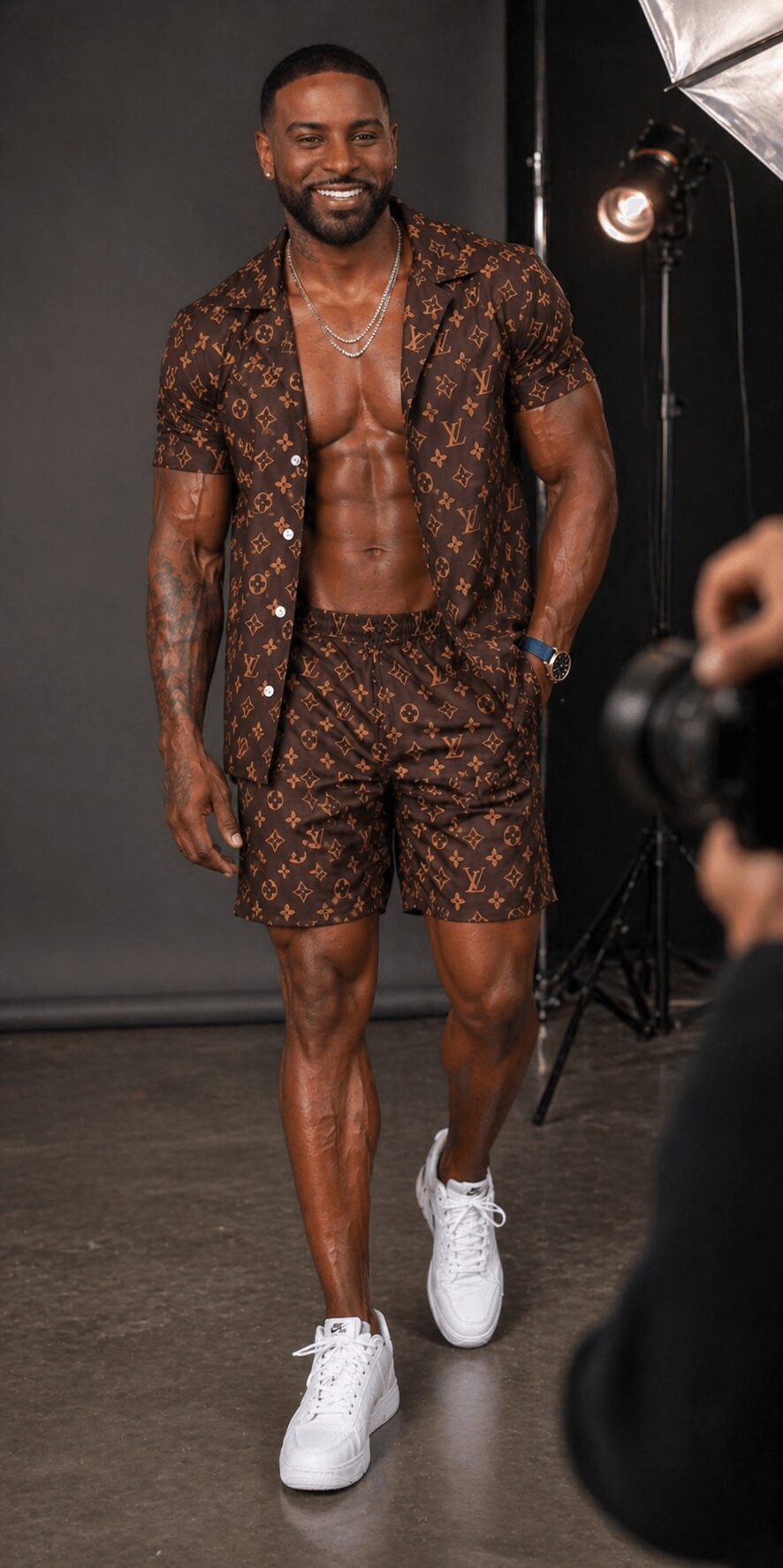 Man walking on runway wearing patterned shirt and shorts, smiling, with studio lighting in background.