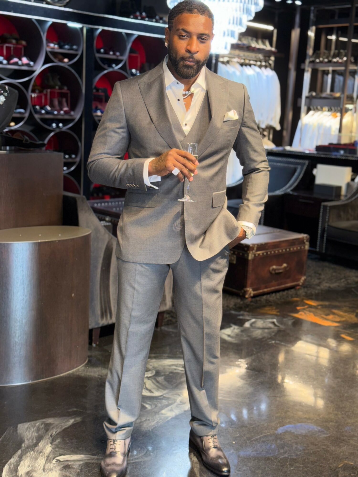 Man in a gray suit standing in a store with wine bottles and shelves behind him.