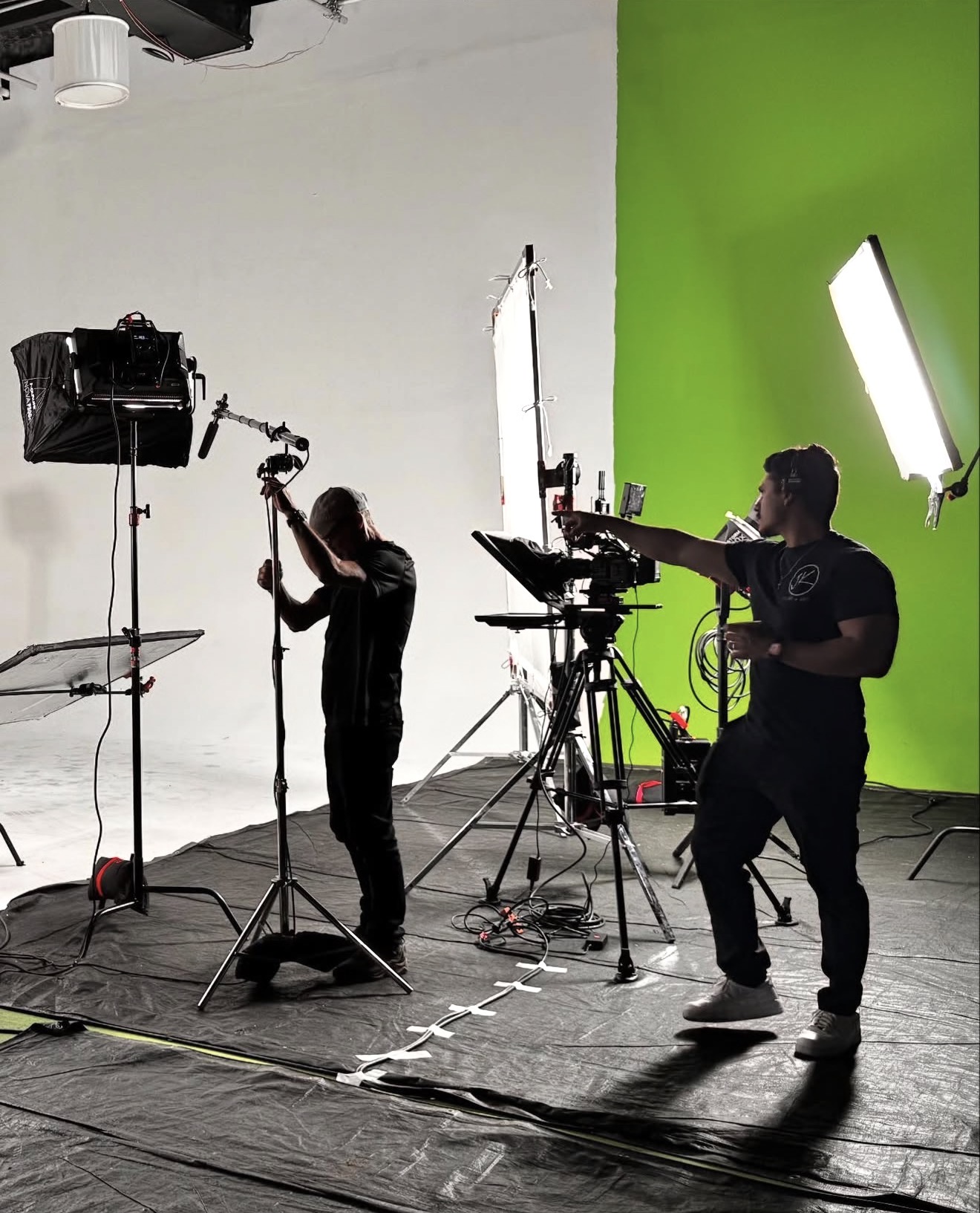 Studio with crew members, camera, and lighting equipment in front of a white and green screen backdrop.