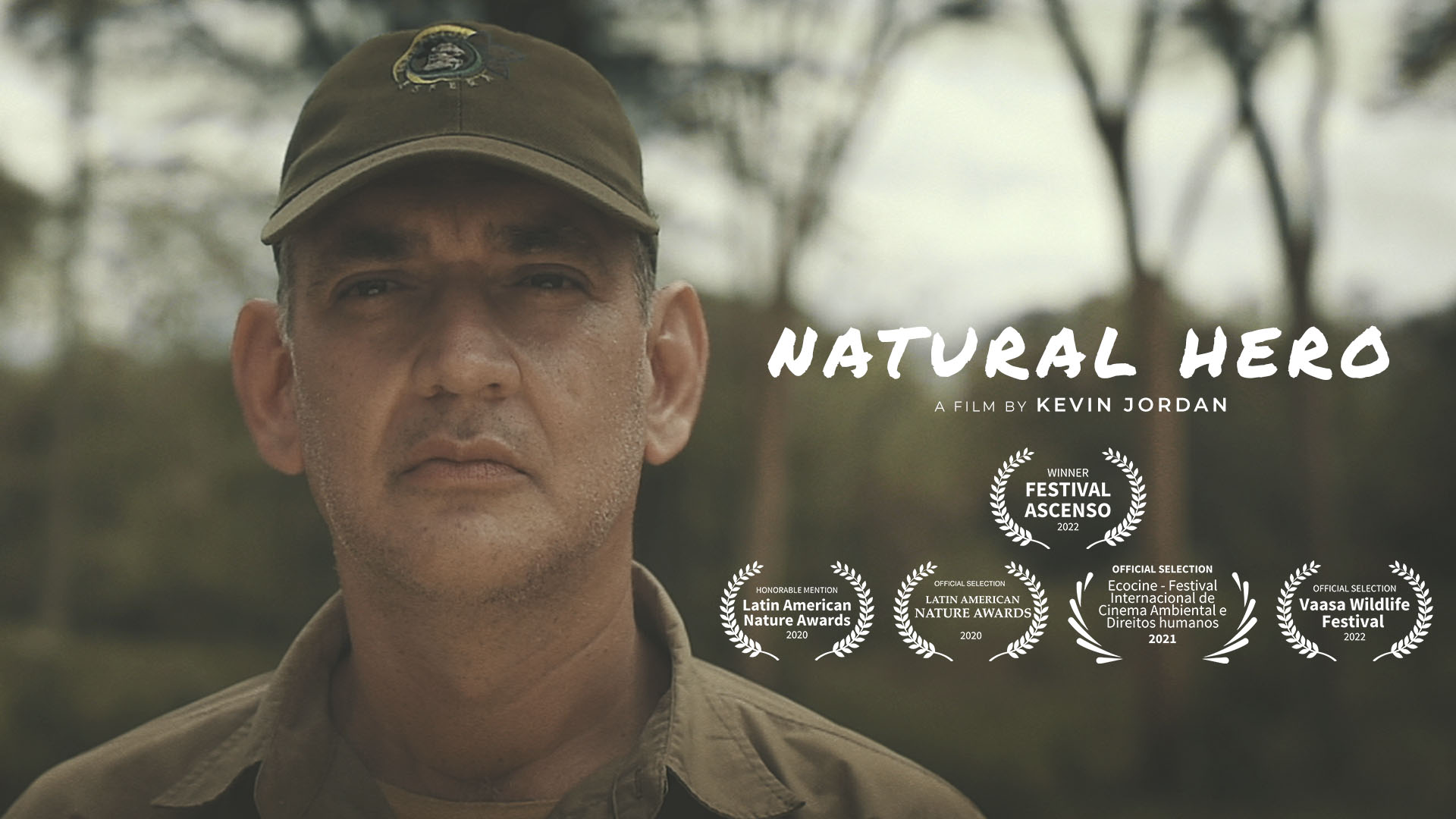 Close-up of a man wearing a cap outdoors with trees in the background, with text 'Natural Hero' and award symbols.