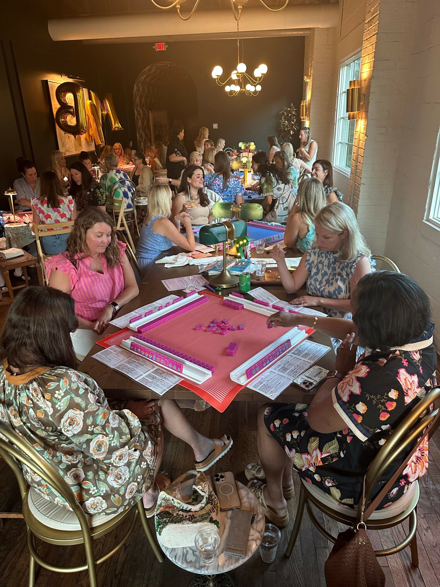 People gathered around a table with pink paper, writing and discussing, in a decorated indoor setting.