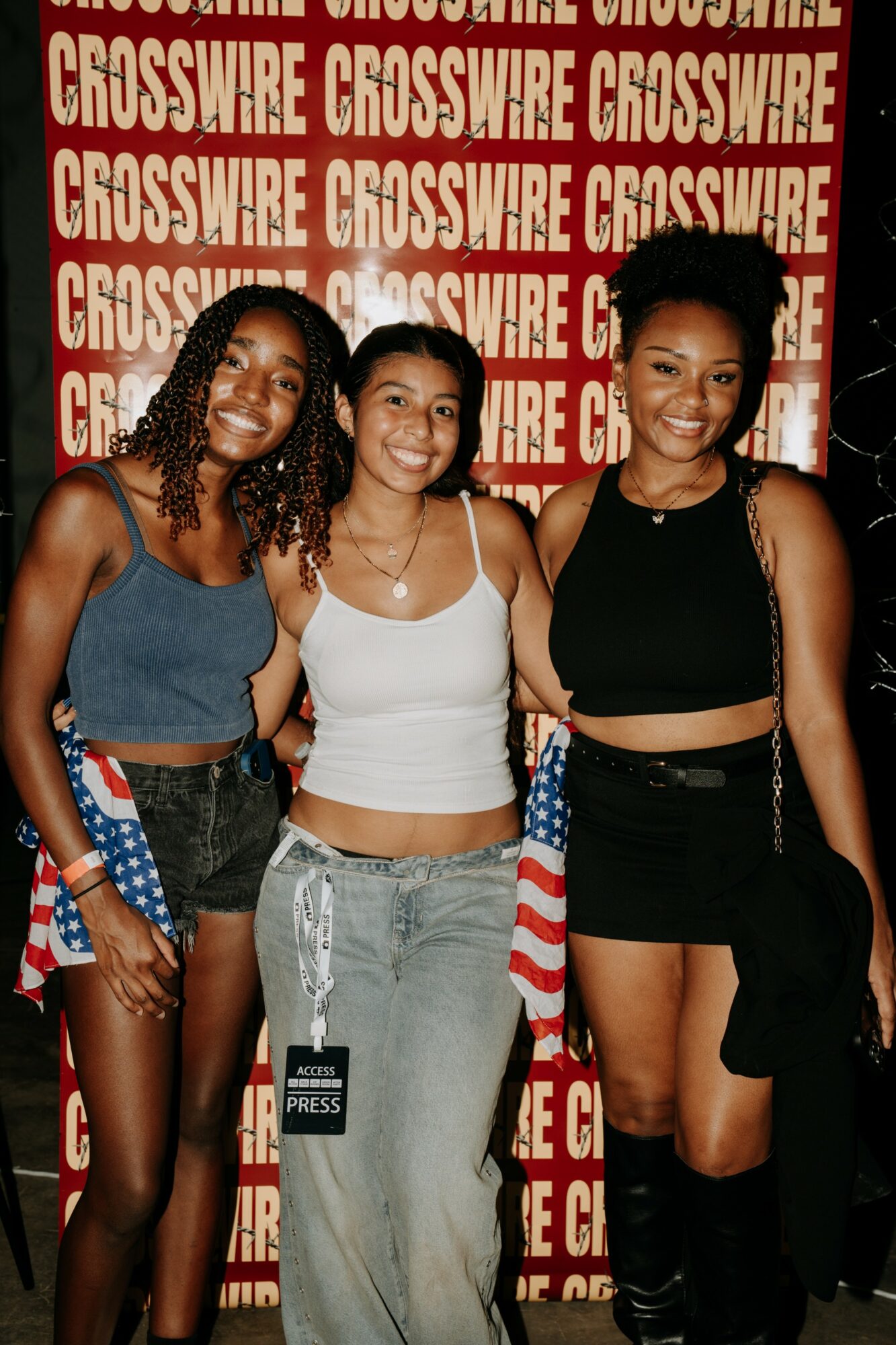Three young women smiling in front of a red background with white text, wearing casual outfits and accessories.