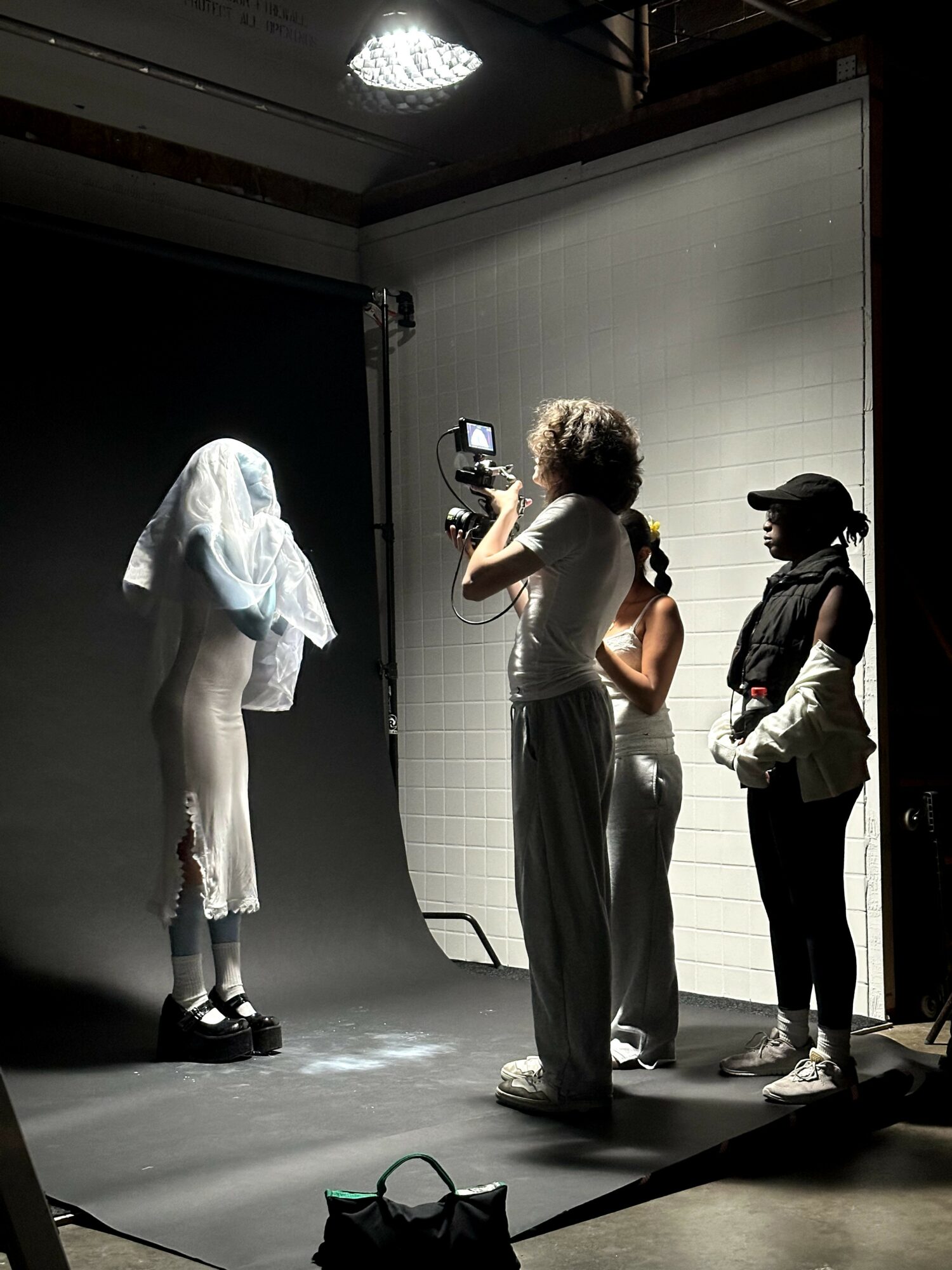Person with a camera filming a person with a cloth over their head, in a studio setting.