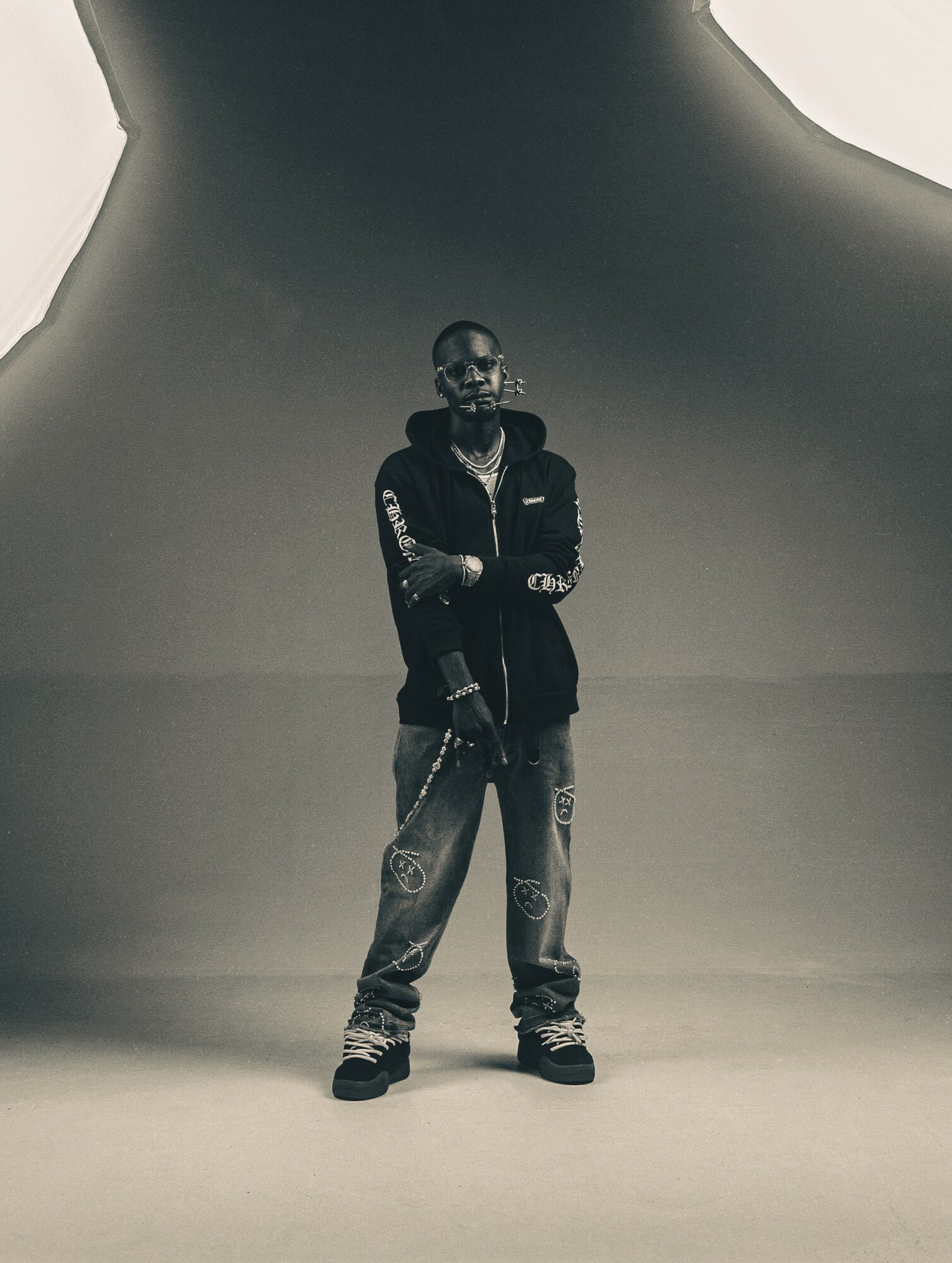 Person standing with arms crossed in a studio with a large, curved backdrop, in black and white.