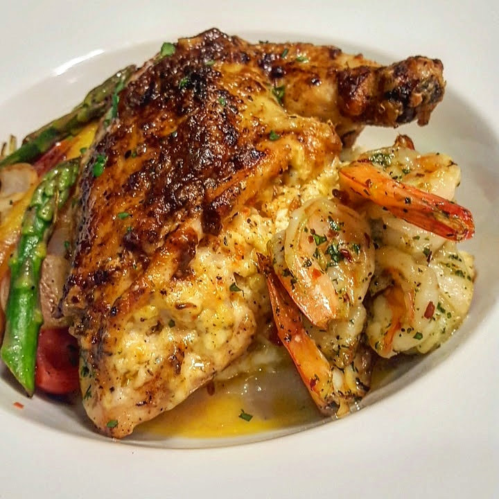 Grilled chicken leg with shrimp and vegetables on a white plate.