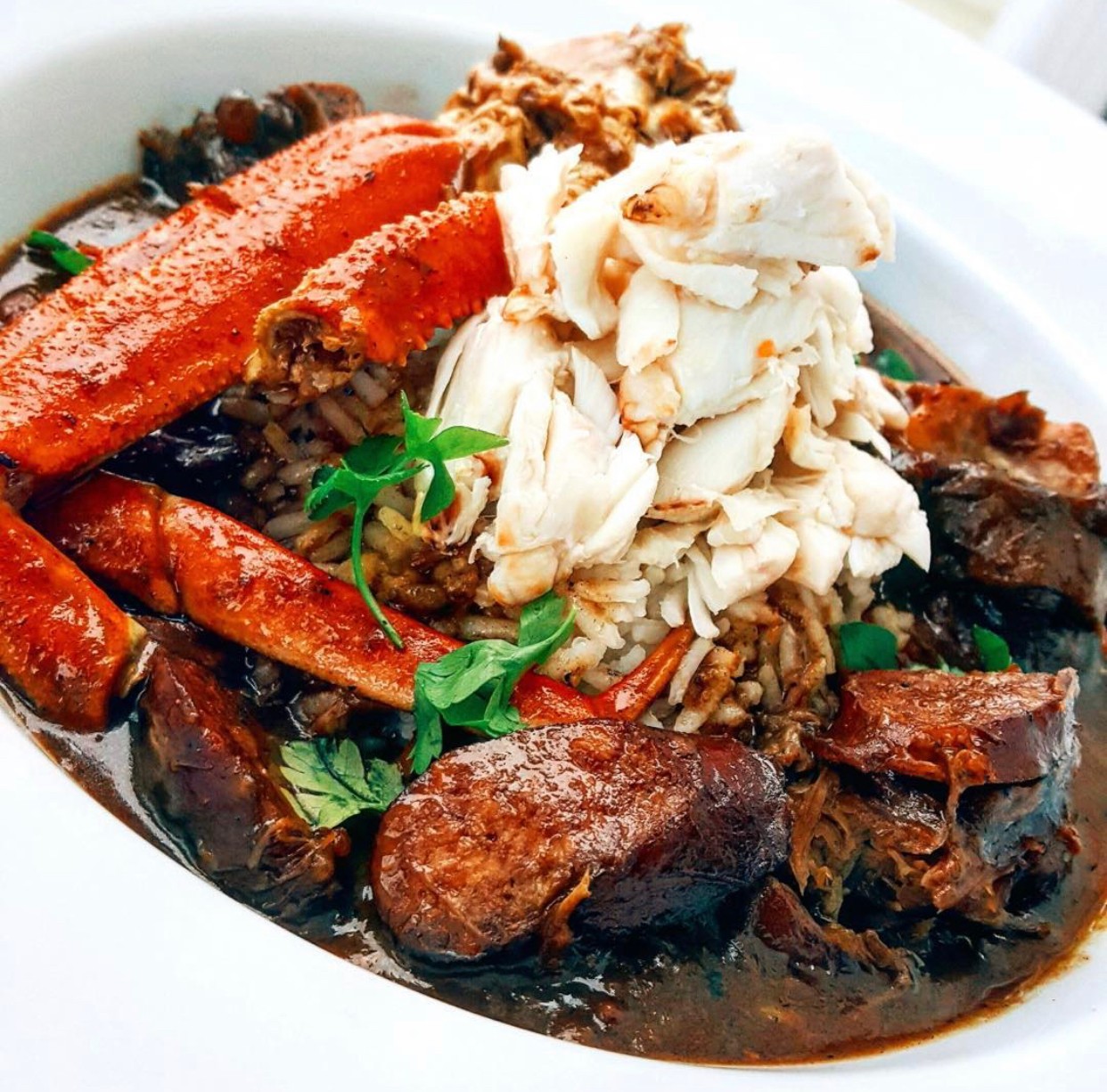 Dish with rice, vegetables, and meat, garnished with herbs in a white bowl.