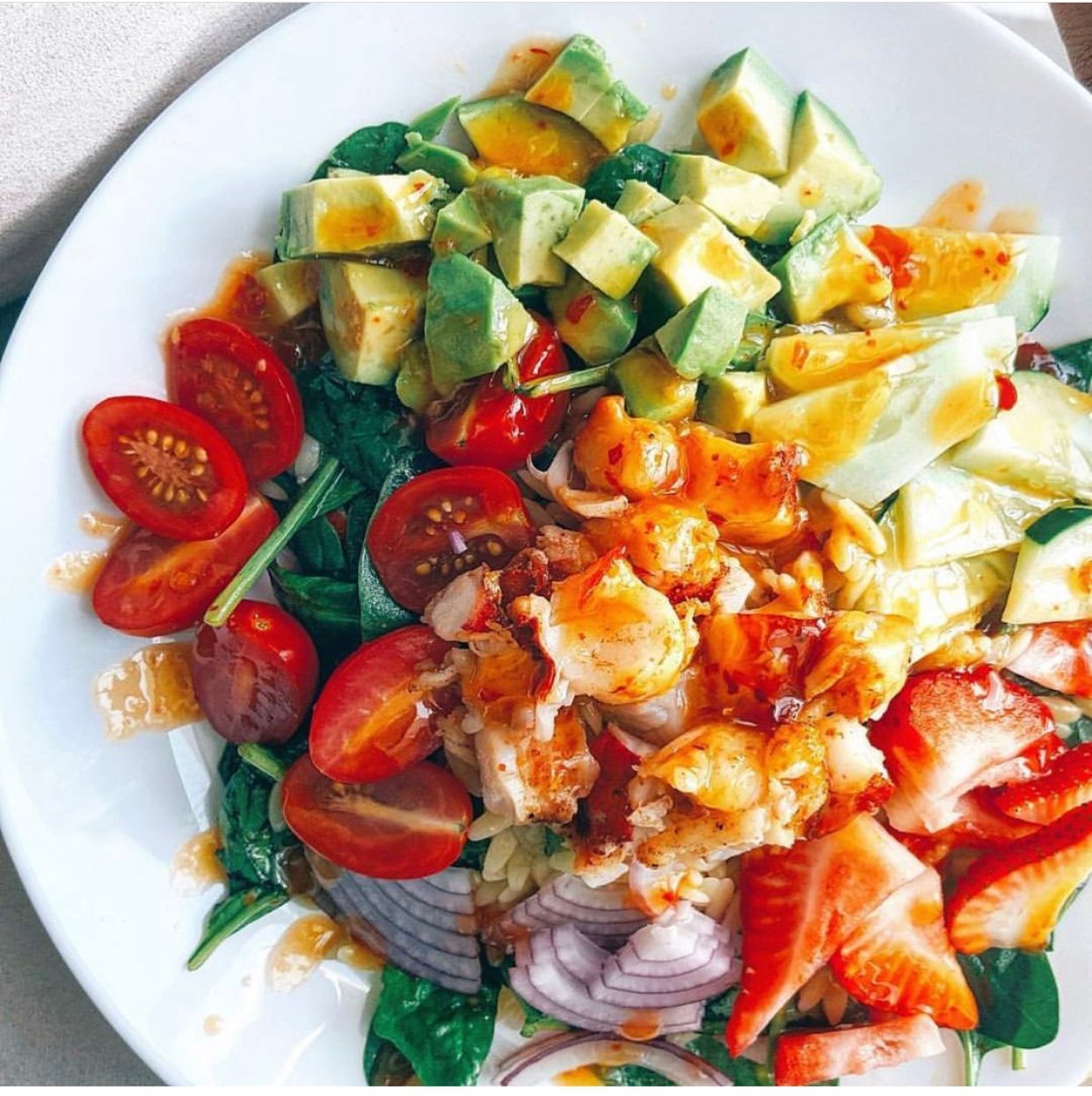 Salad with cherry tomatoes, avocado, strawberries, cucumbers, and onions on a white plate.