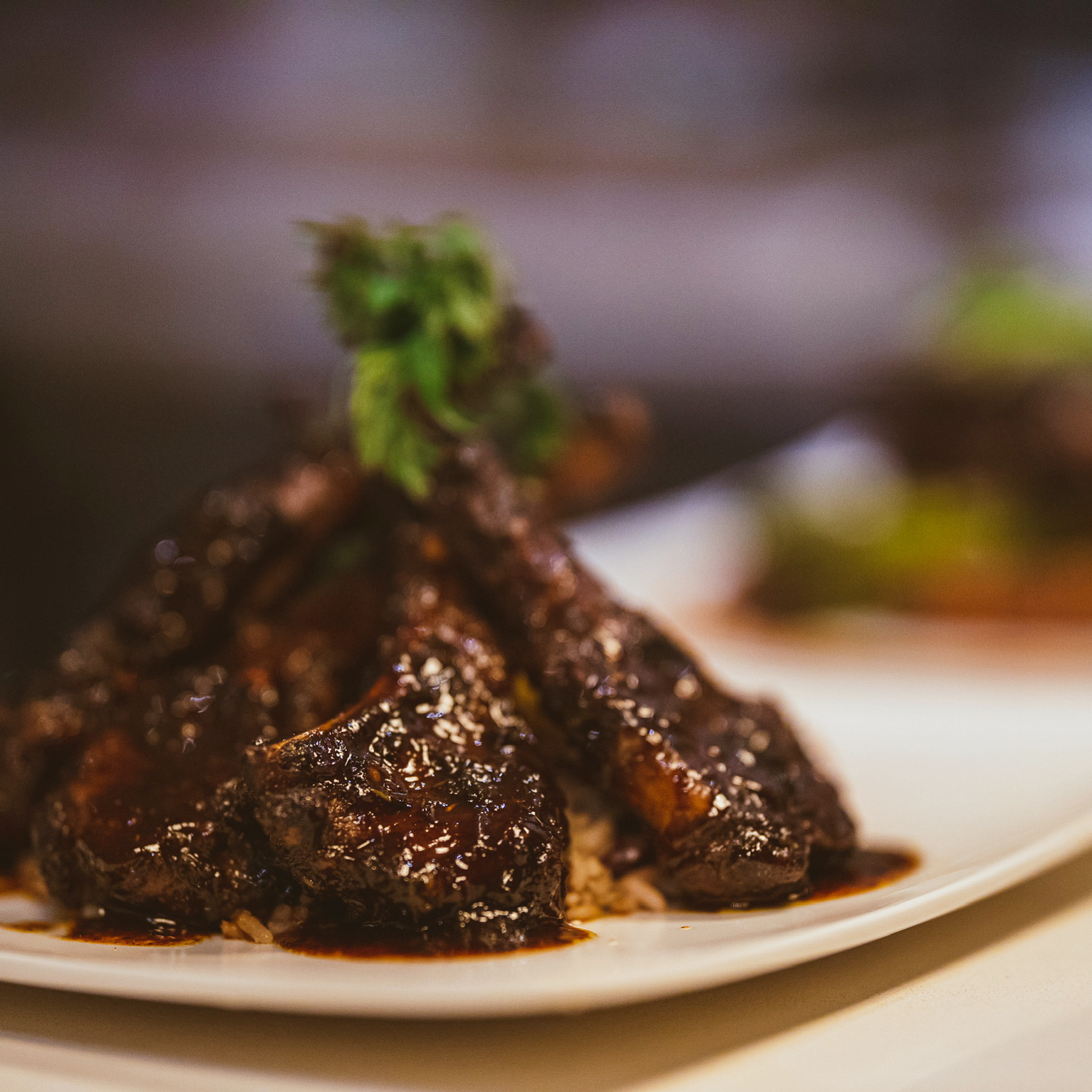 Close-up of glazed meat pieces garnished with a small green herb on a white plate.