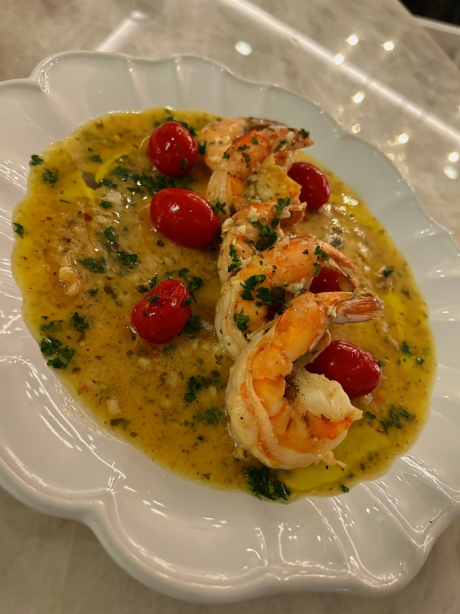 Shrimp and cherry tomatoes in a yellow sauce with herbs on a white dish