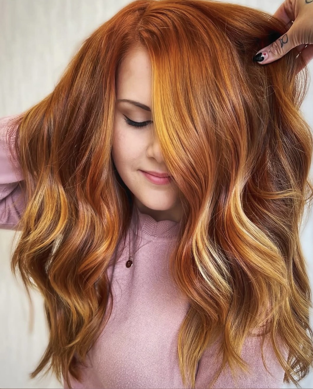 Woman with long, wavy red hair covering part of her face, wearing a pink top, looking down.