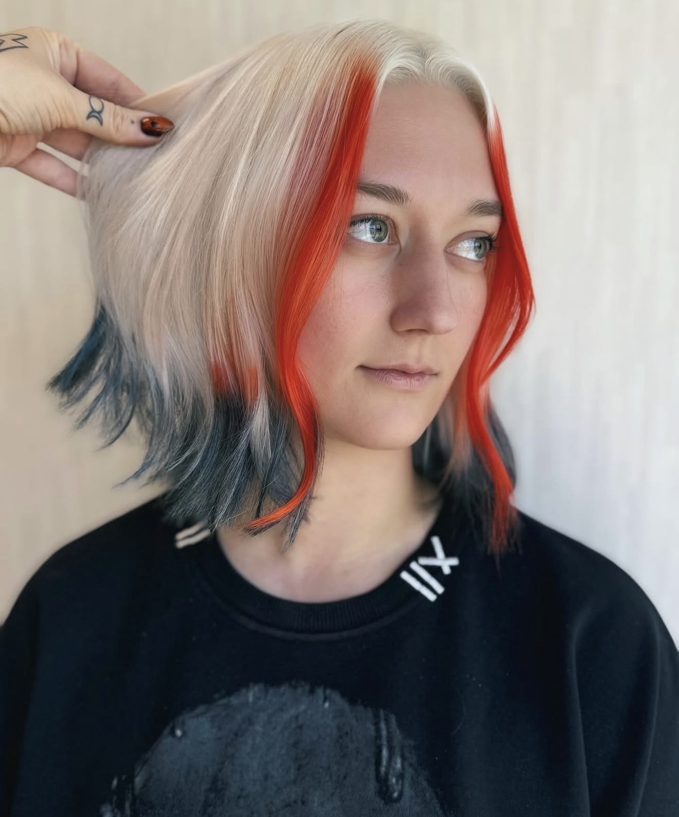 Young woman with multicolored hair, including blonde, red, and dark blue sections, looking to the side.