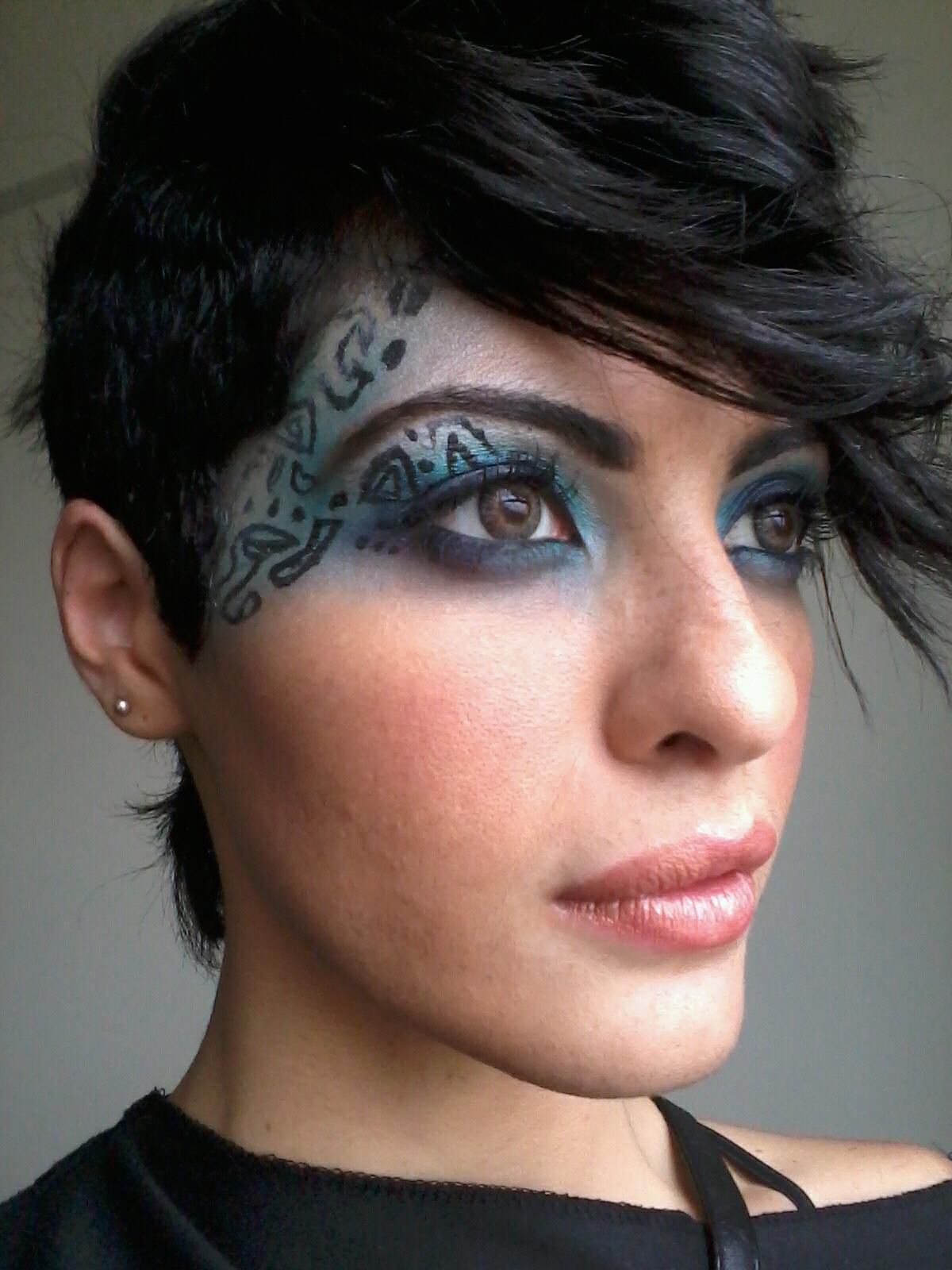 Woman with short dark hair, blue eye makeup, and face tattoo, looking to the side.