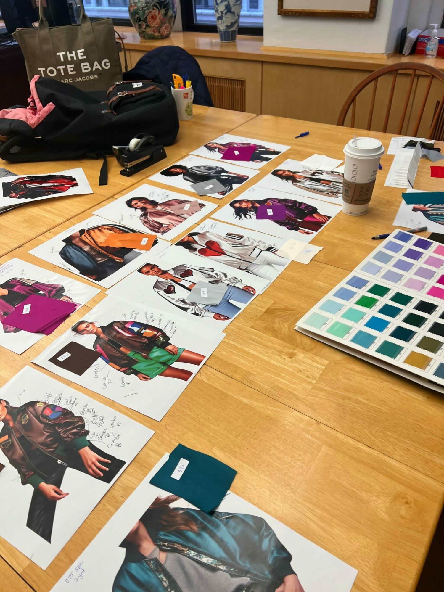Table with fabric swatches, color palette, and fashion sketches, along with a person's arm and a bag on the table.
