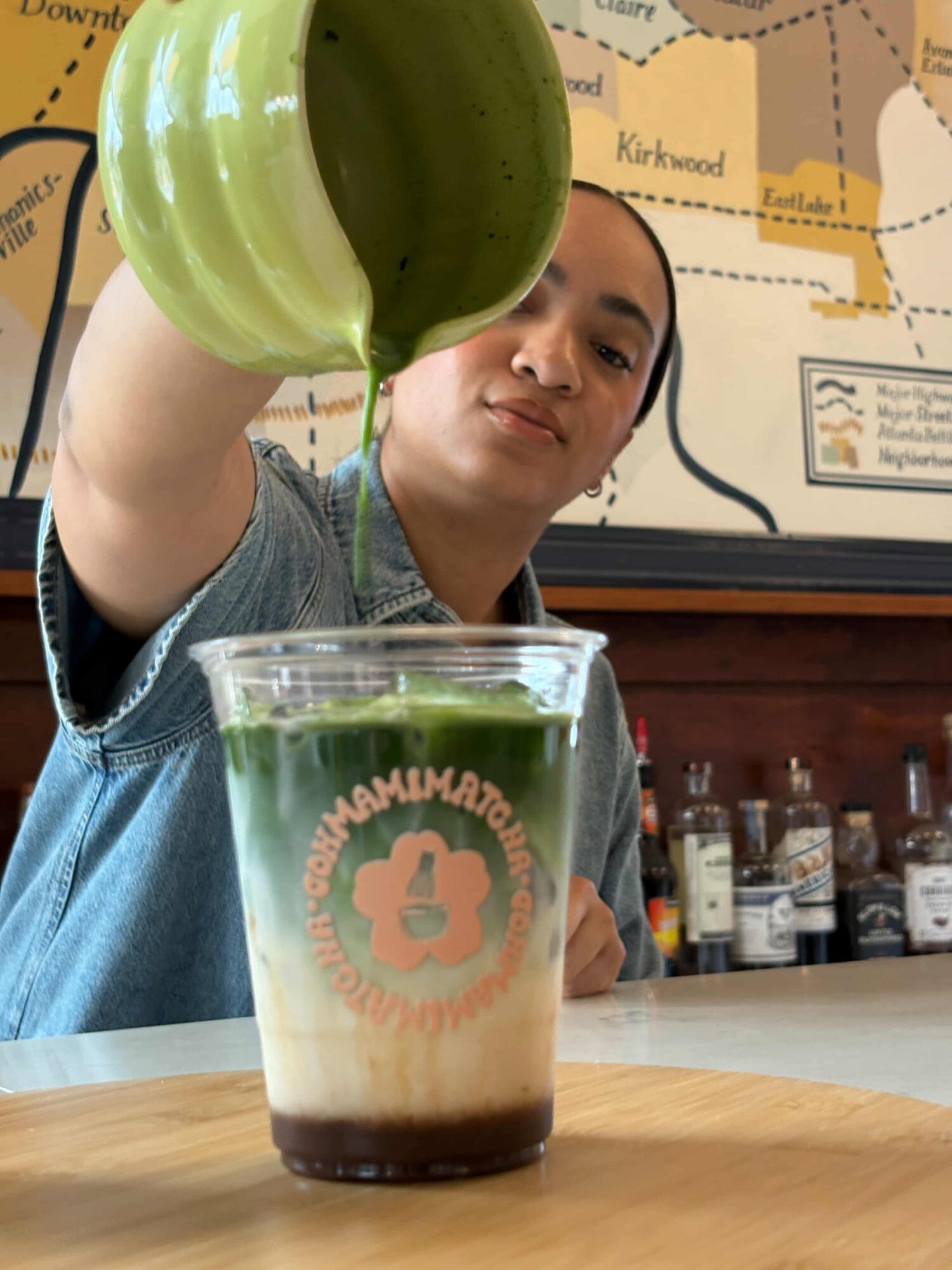 Person pouring green liquid into a layered drink with a map in the background.