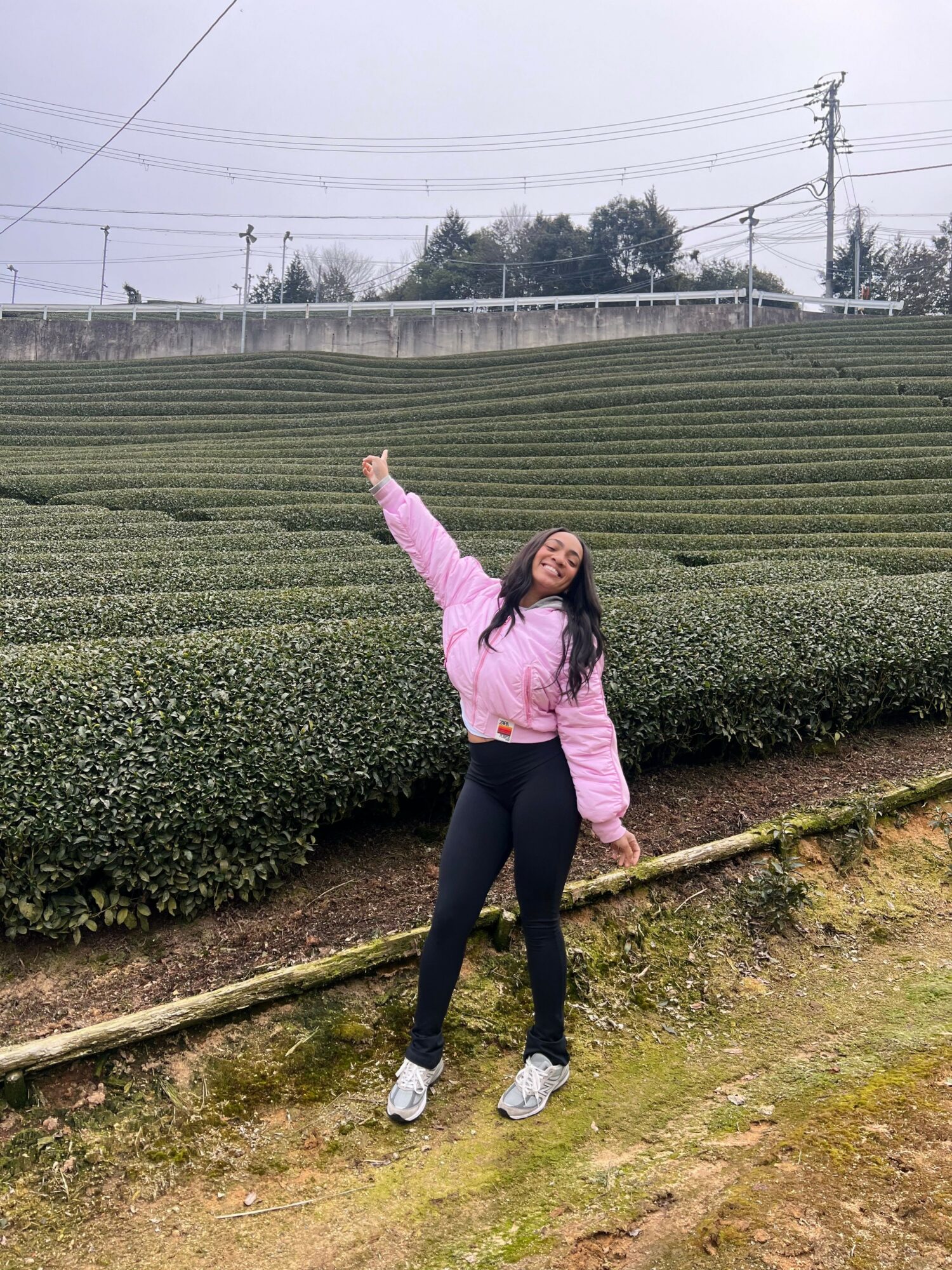 Person standing on a narrow strip of land with greenery and power lines in the background.