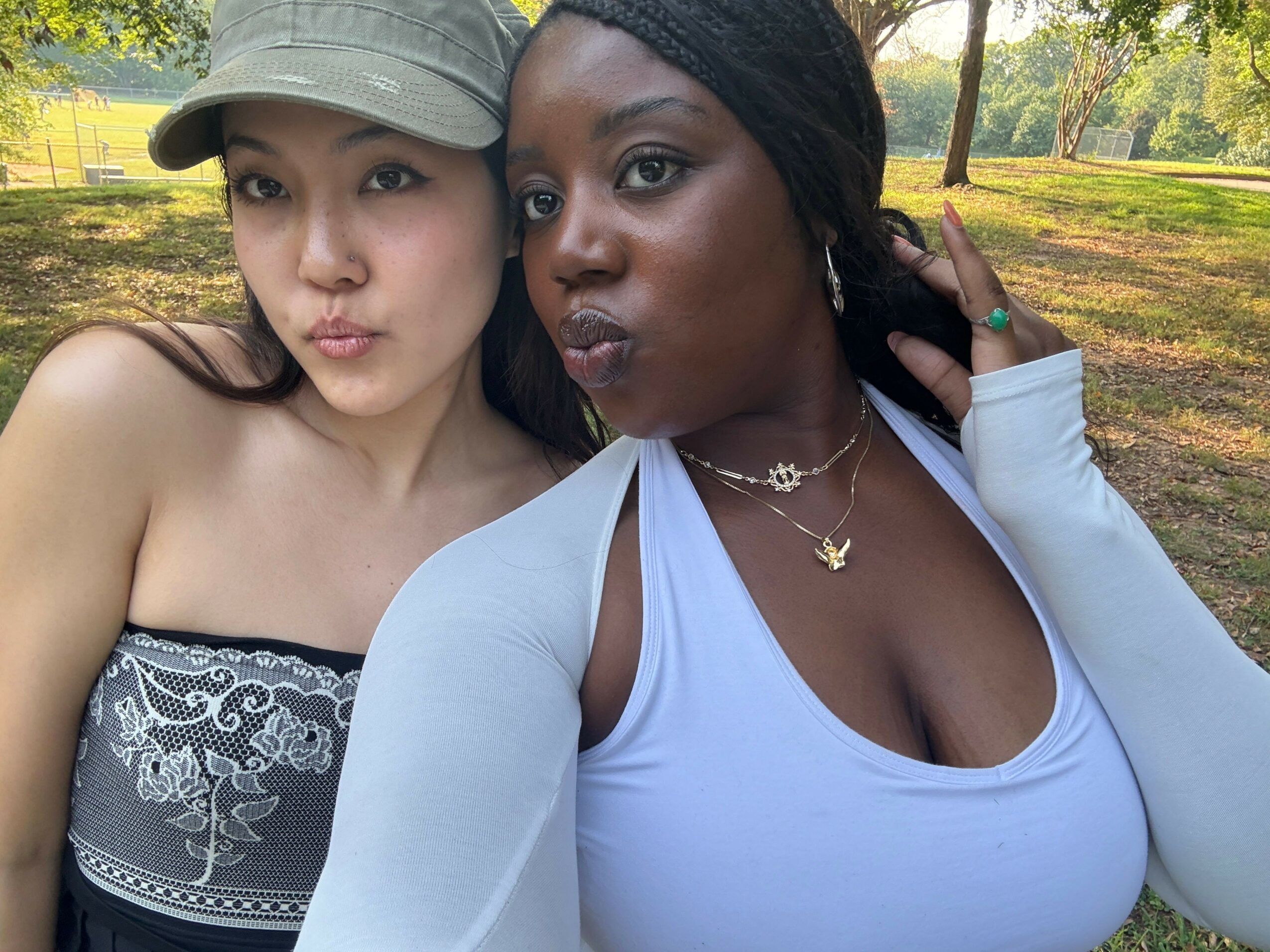 Two women lying outdoors, facing the camera, with trees and grass in the background.