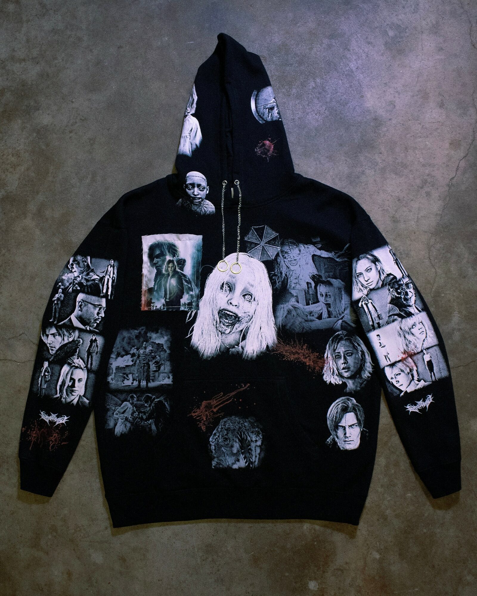 Black hoodie with various horror-themed images and faces printed on it, laid flat on a surface.
